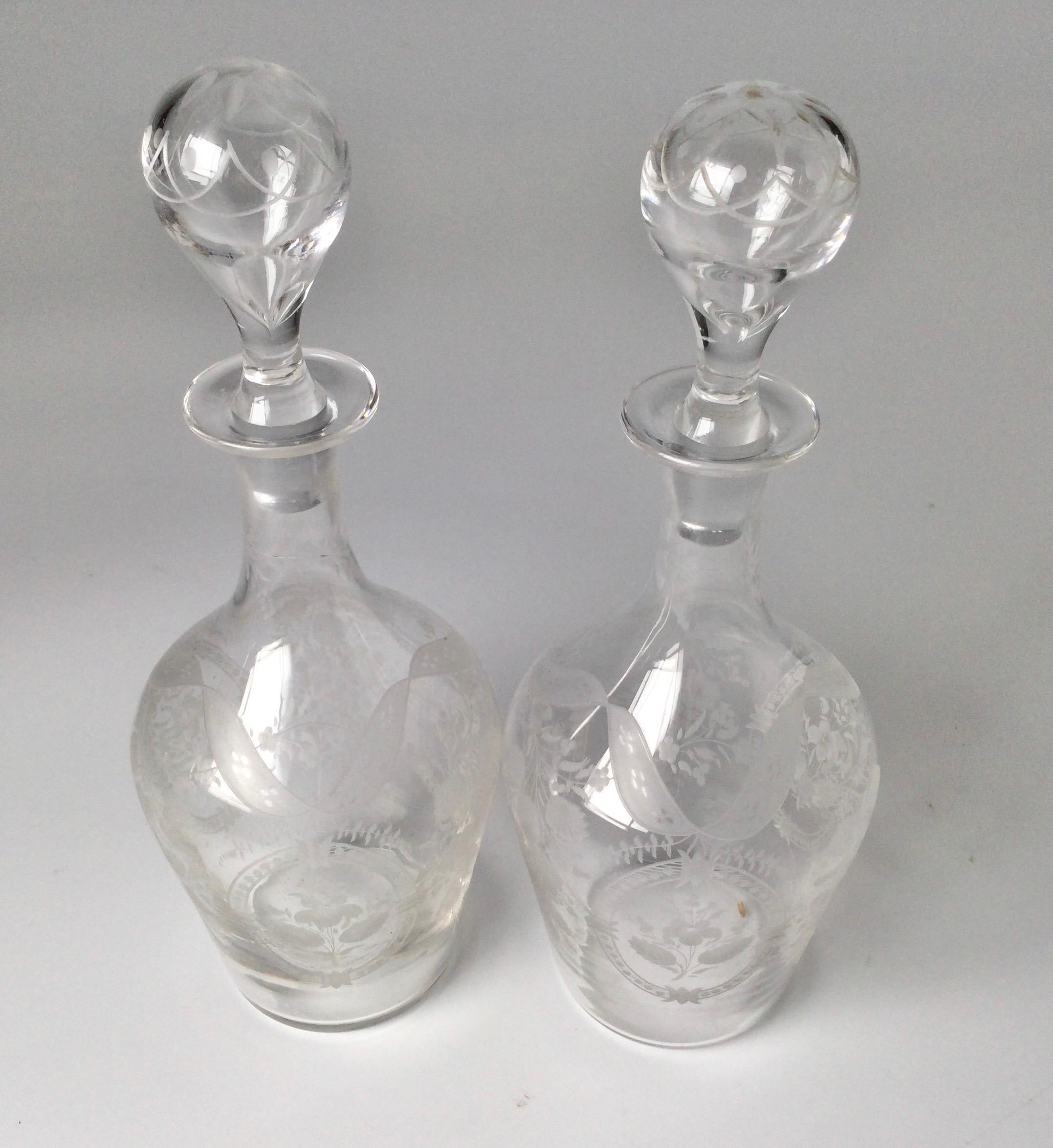 A pair of European hand blown decanters with original stoppers with delicate floral cartouches and garland decoration.