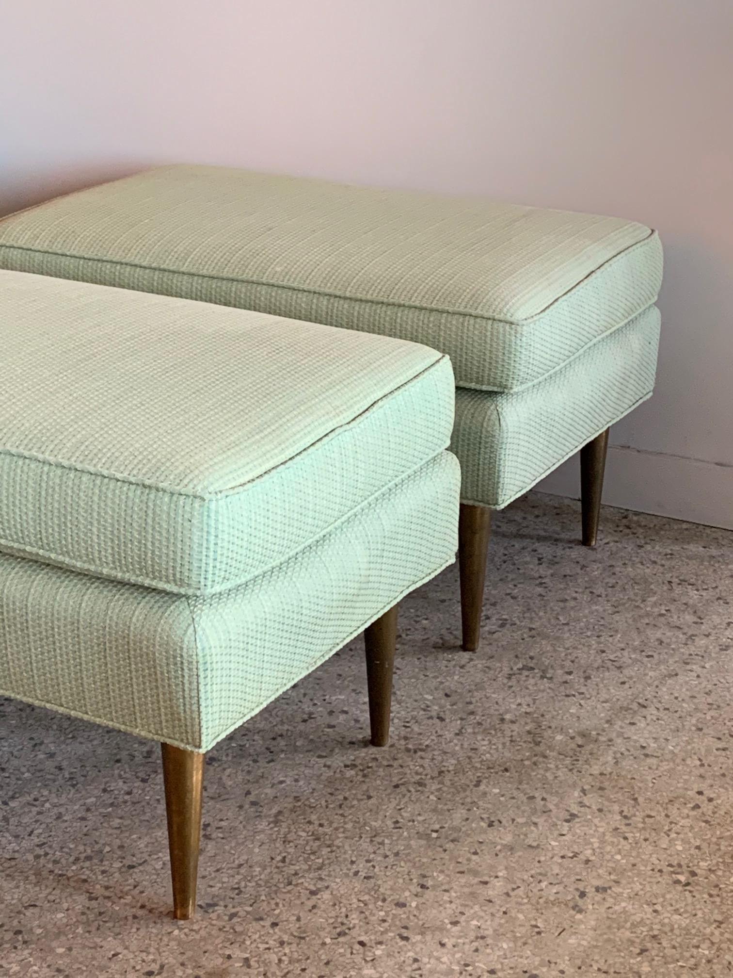 A pair of Classic midcentury ottomans or foot stools. Very heavy and thick brass legs, in the style of Dunbar.