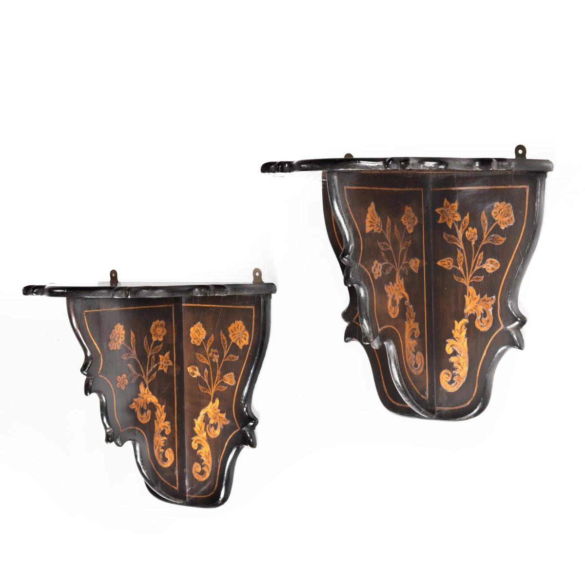 A pair of Dutch marquetry wall brackets, each with a triangular serpentine top, a similar shaped back and central support, decorated overall with a gilt-painted single linear border on an ebonized ground, the supports inlaid with carnation sprays