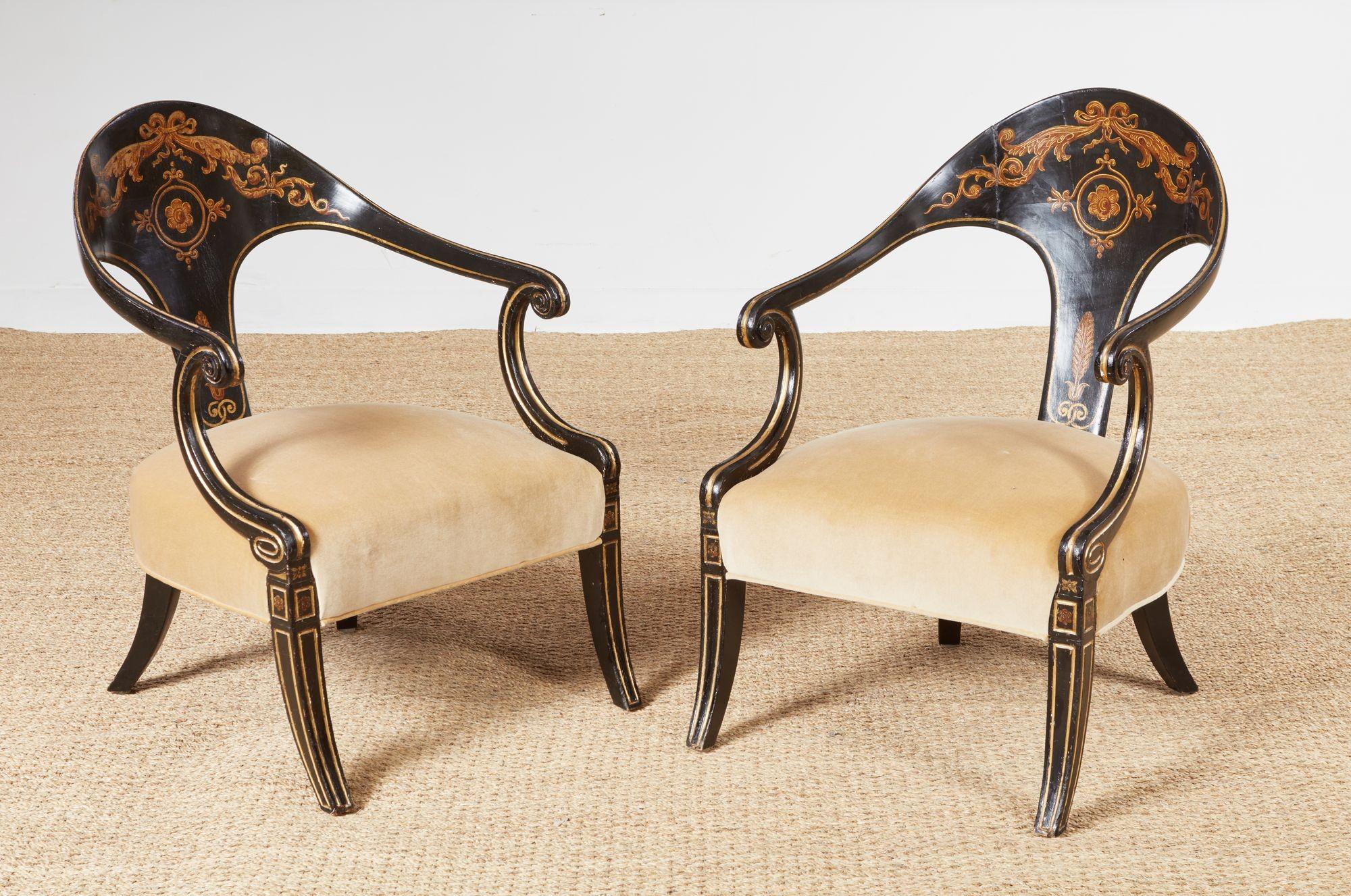 A rare pair of period English Regency spoonback chairs with distinctive inwardly curved back and integral downswept arms over upholstered seats on sabre legs. Elaborate hand-painted ebonized decoration with gilt highlights. English, circa 1820. 31