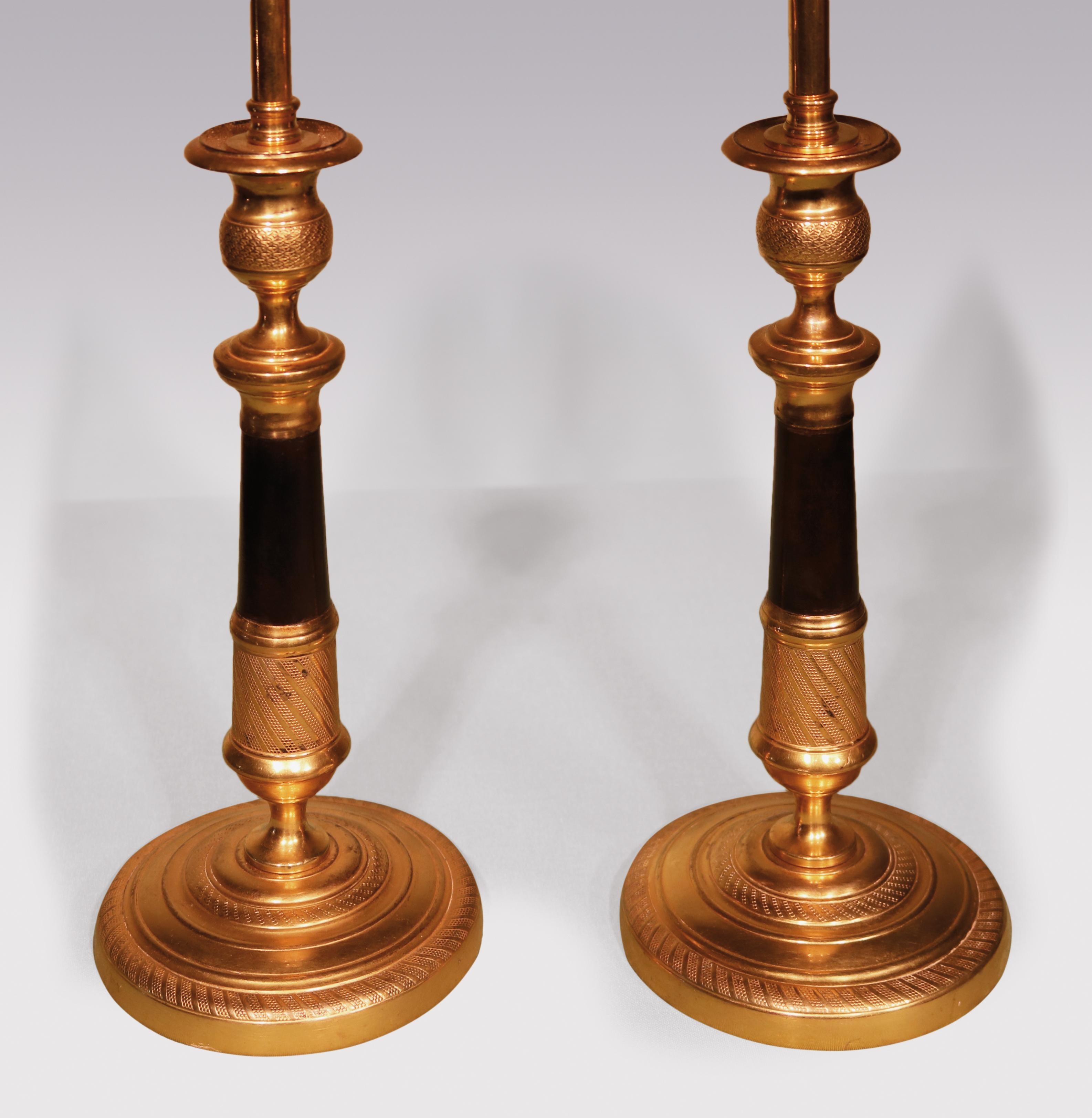 A pair of early 19th century bronze & ormolu Candlesticks, having fishscale engine-turned sconces above tapering stems with spiral engine-turning supported on circular bases.

(Now converted to lamps).