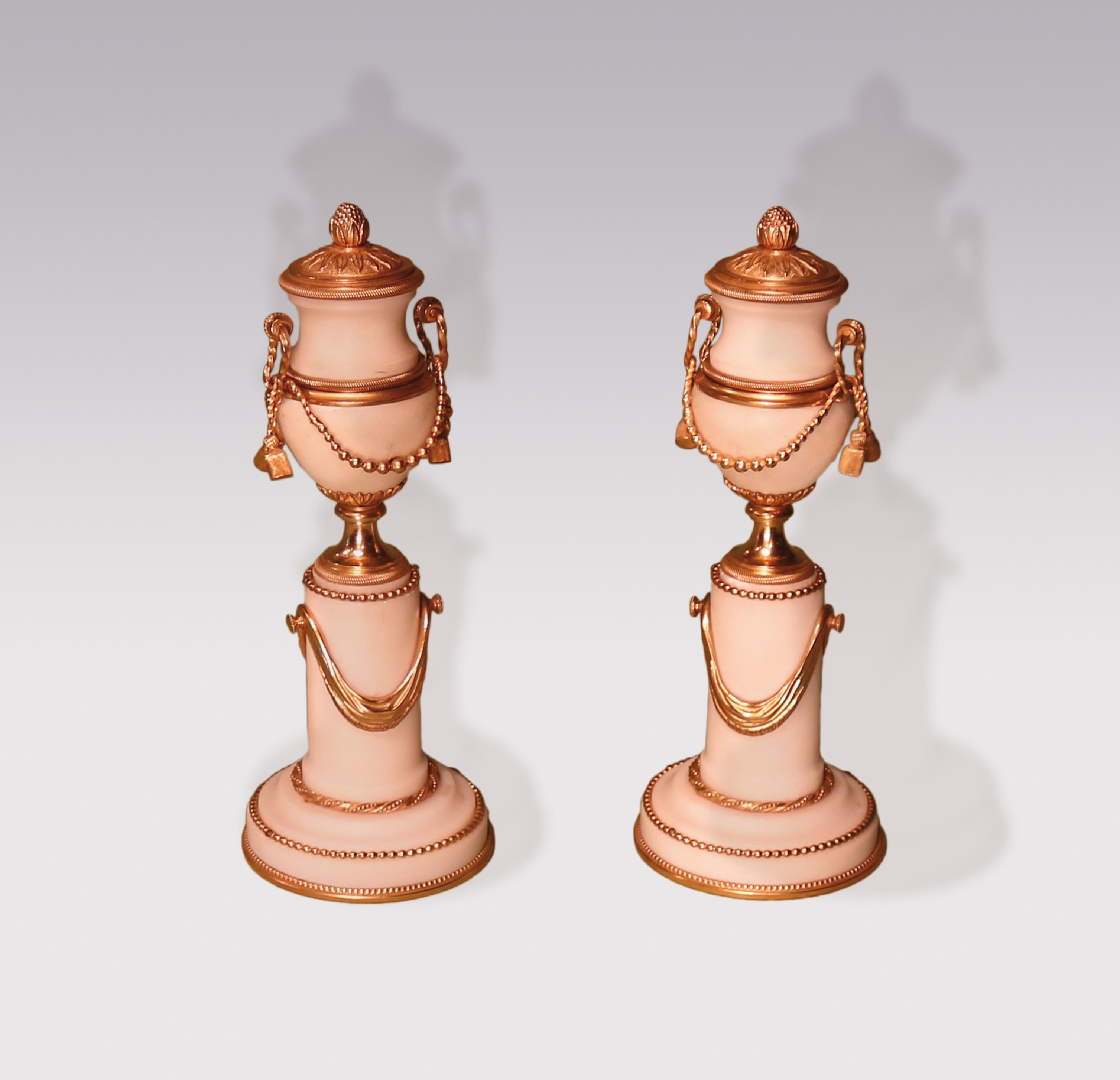 A pair of early 19th century white marble and ormolu cassolettes. Having pineapple finial lids converting to candle holders, decorated with beaded swags with tassels, supported on columns with applied swags, ending on circular bases.
