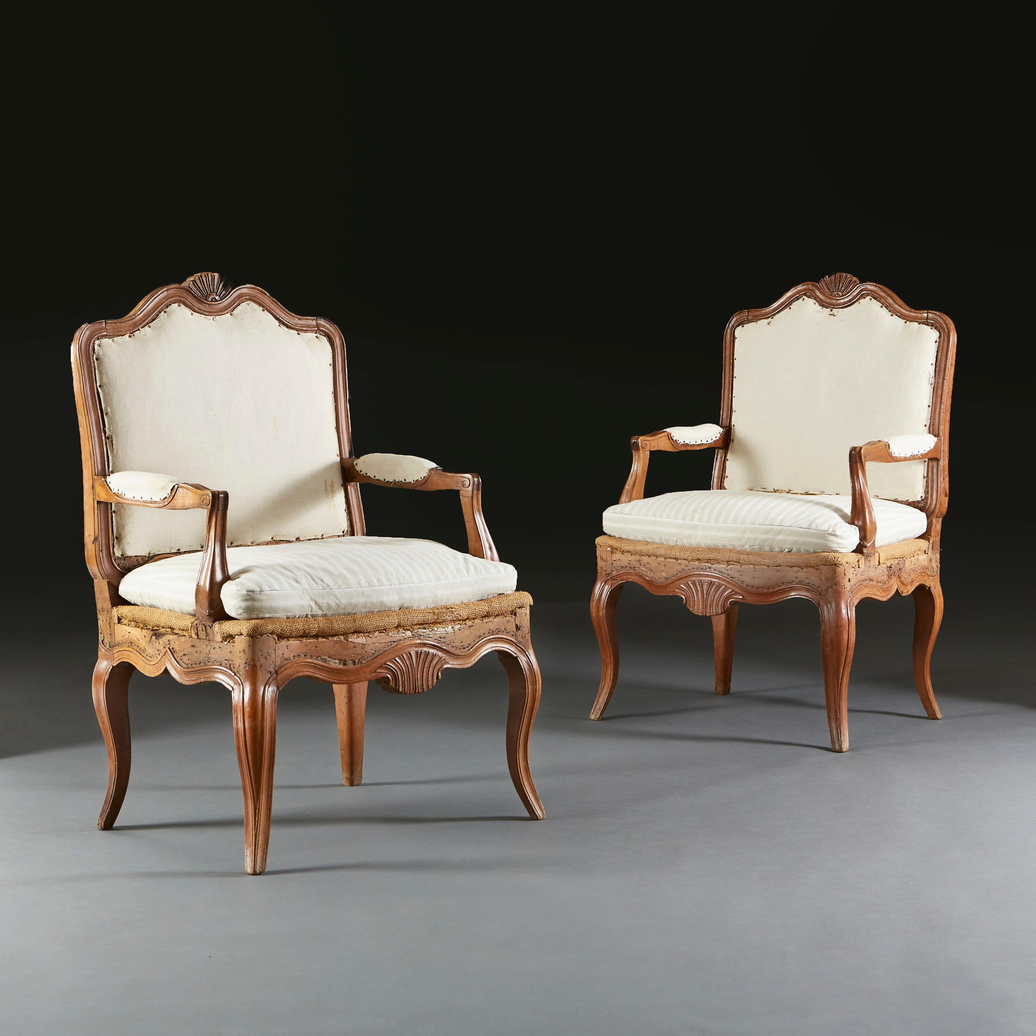 A pair of early nineteenth century walnut open armchairs with carved shells to the back seat rail, upholstered seats, all supported on four cabriole legs.