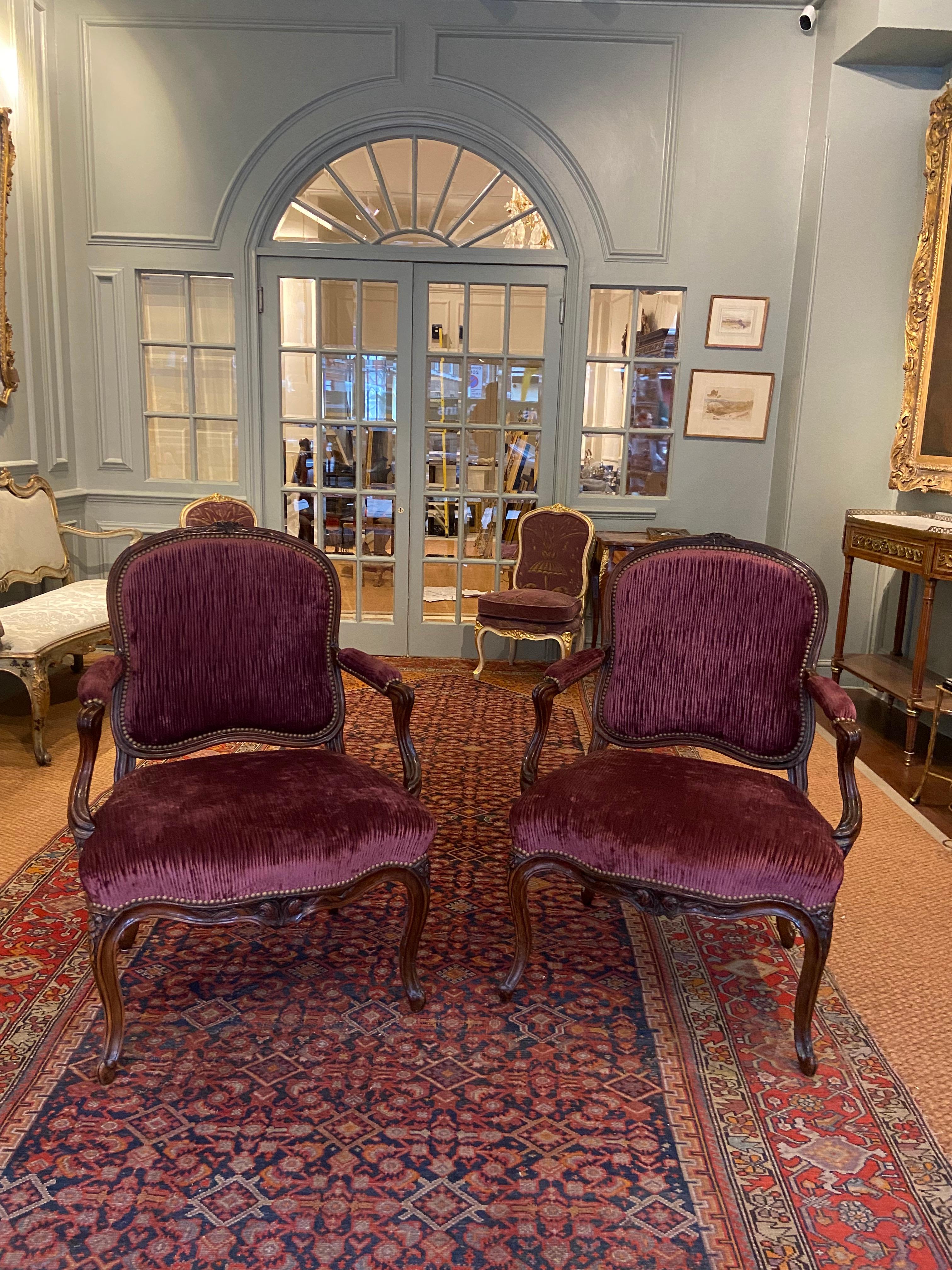 A pair of Early Provincial Louis XV walnut fauteuils (open armchairs) (Mid 18th Century). Stamped Nougaret. Each with cartouche-shaped padded back, arms and serpentine-fronted seat, upholstered à chassis in plum velvet, Channelled frame with central