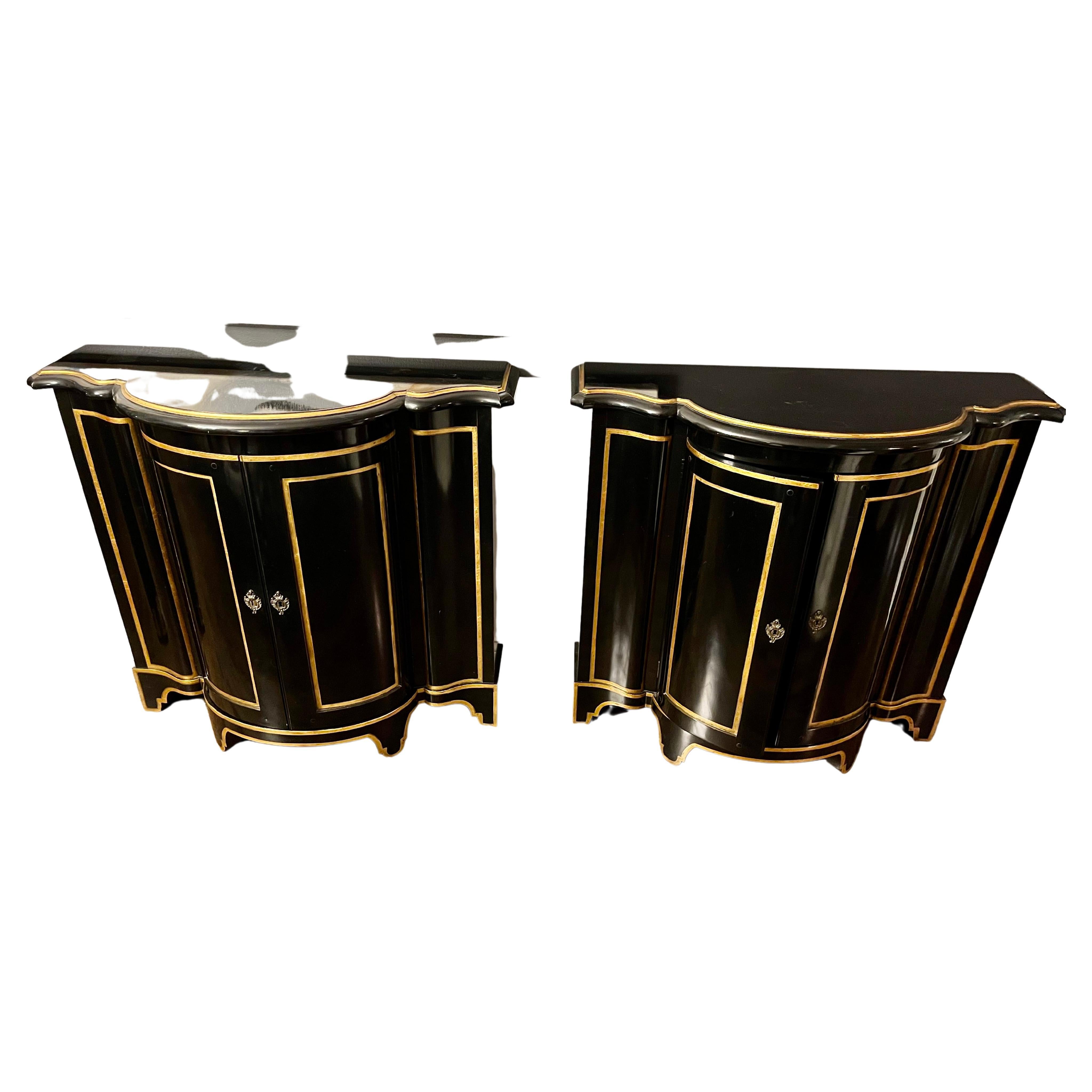 A pair of ebonized and gilt demi-lune cabinets with gilt accents by Baker Furniture Company. Each having two doors when opened revealing a shelf and the Baker Furniture Company metal placque.