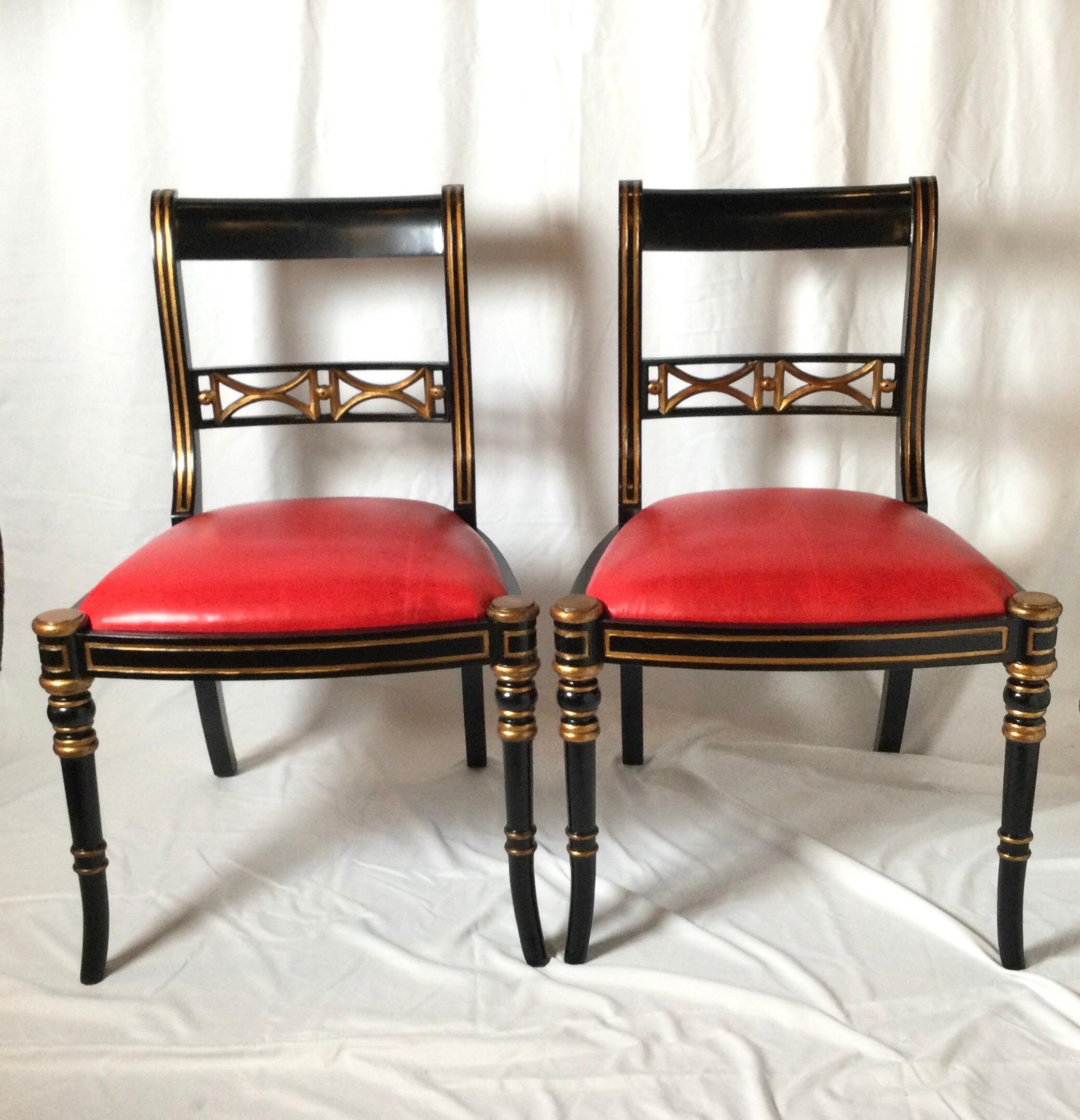 A pair of black and gilt Regency style side chairs with new red leather seats. Elegant frames with gold highlighted details.
