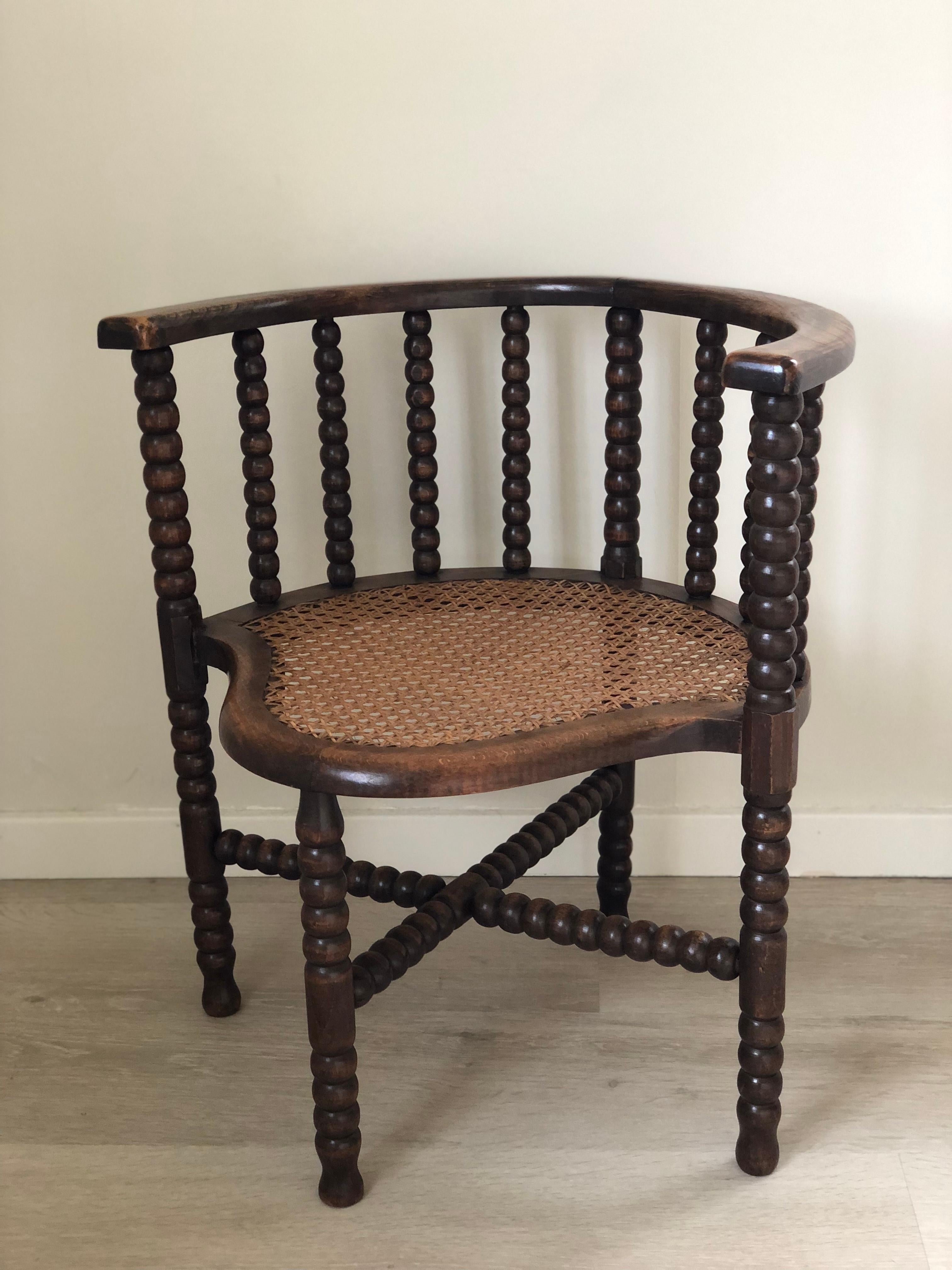 Questa elegante coppia di poltrone edoardiane, realizzate nel Regno Unito all'inizio del XX secolo, presenta un classico design a spola. Realizzata in faggio massiccio, ogni sedia è dotata di un sedile in canna intrecciata e presenta gambe e