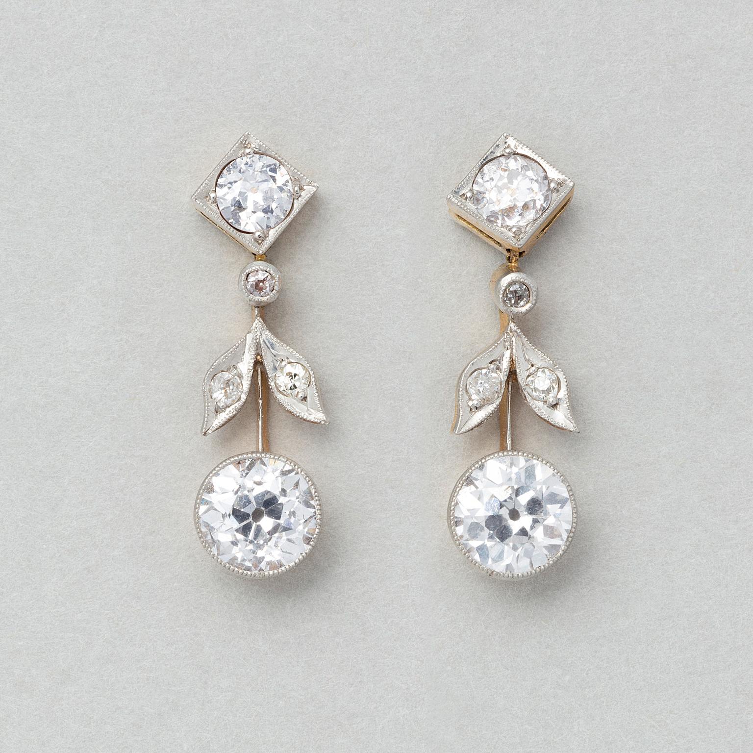 A pair of Edwardian platinum and yellow gold earrings on the ear a diamond shape mille griffe set with an old cut diamond (each app. 0.2 carat) with three small old cut diamonds, set in leaves and below that a larger old cut diamond (each app. 0.65
