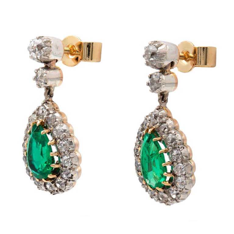 A pair of Edwardian emerald and diamond drop earrings, each earring with a pear-shaped emerald, surrounded by fourteen old European-cut diamonds, all suspended by two graduating old European-cut diamonds, the emeralds estimated to weigh 0.9 carats