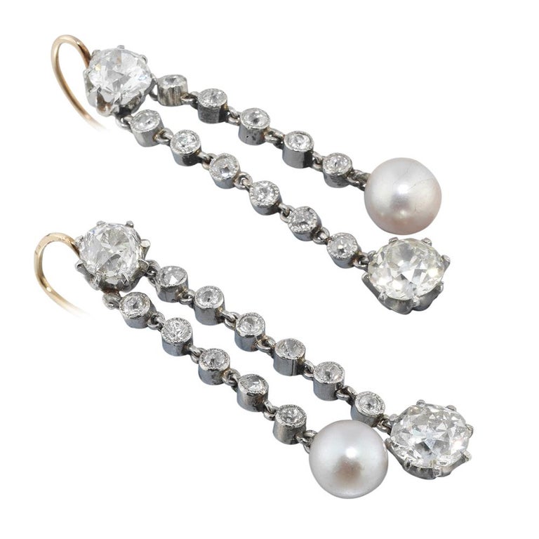 A pair of Edwardian natural pearl and diamond drop earrings, each earring set with an old brilliant-cut diamond surmount, weighing a total of 1.22 carats, suspending two diamond-set chain runs of alternating lengths, with natural pearl and old