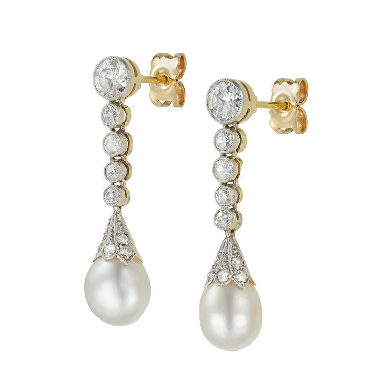 A pair of Edwardian pearl and diamond drop earrings, each earring consisting of a natural drop pearl surmounted from a rose-cut diamond set fluted cap suspended from five graduating old brilliant-cut diamonds, estimated to weigh a total of 1.6