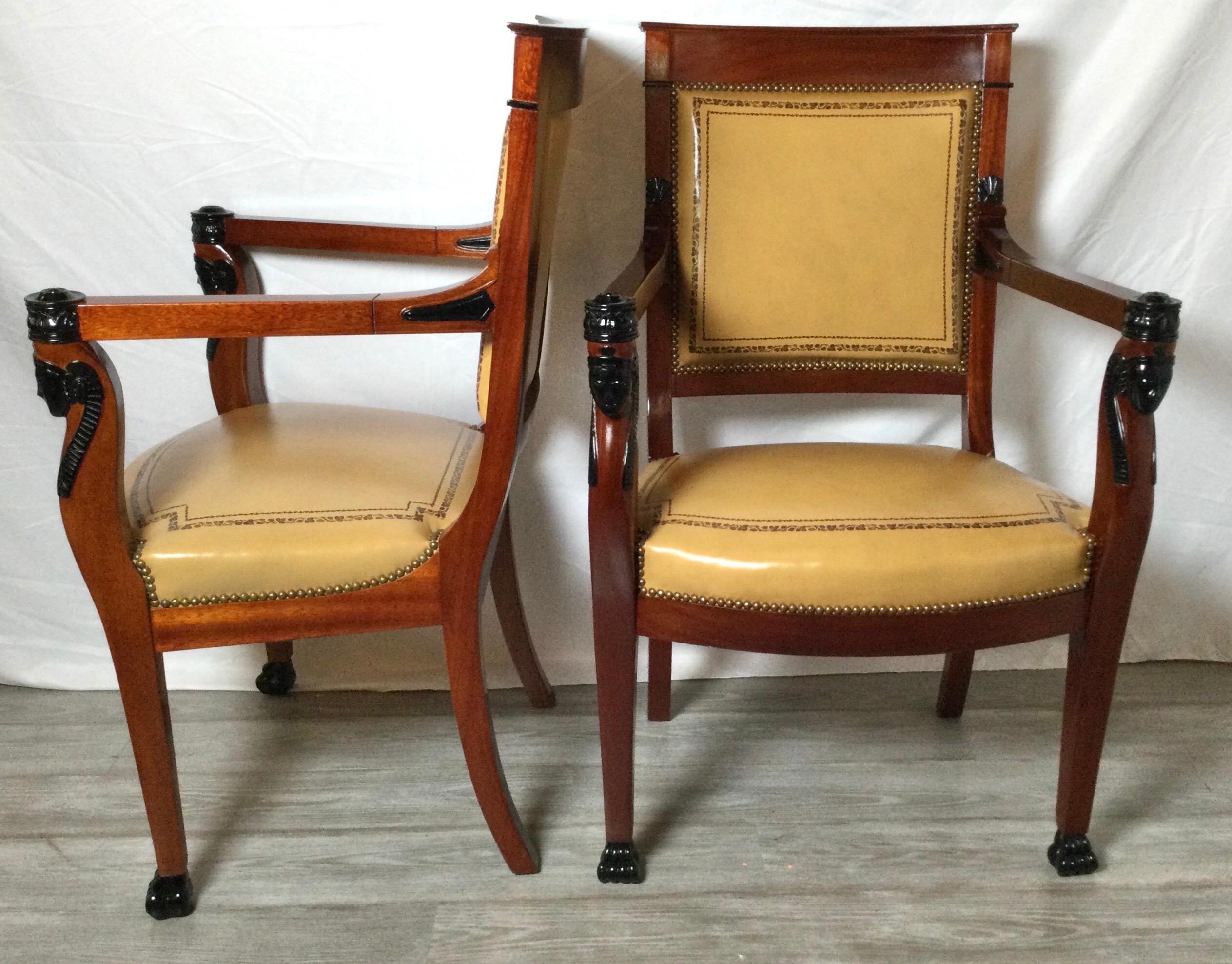A pair of chic leather and mahogany Egyptian Revival open armchairs. The tan leather seats with tooled gilt trim on the seats and backs. The rich mahogany frames with ebonized wood carve accents.