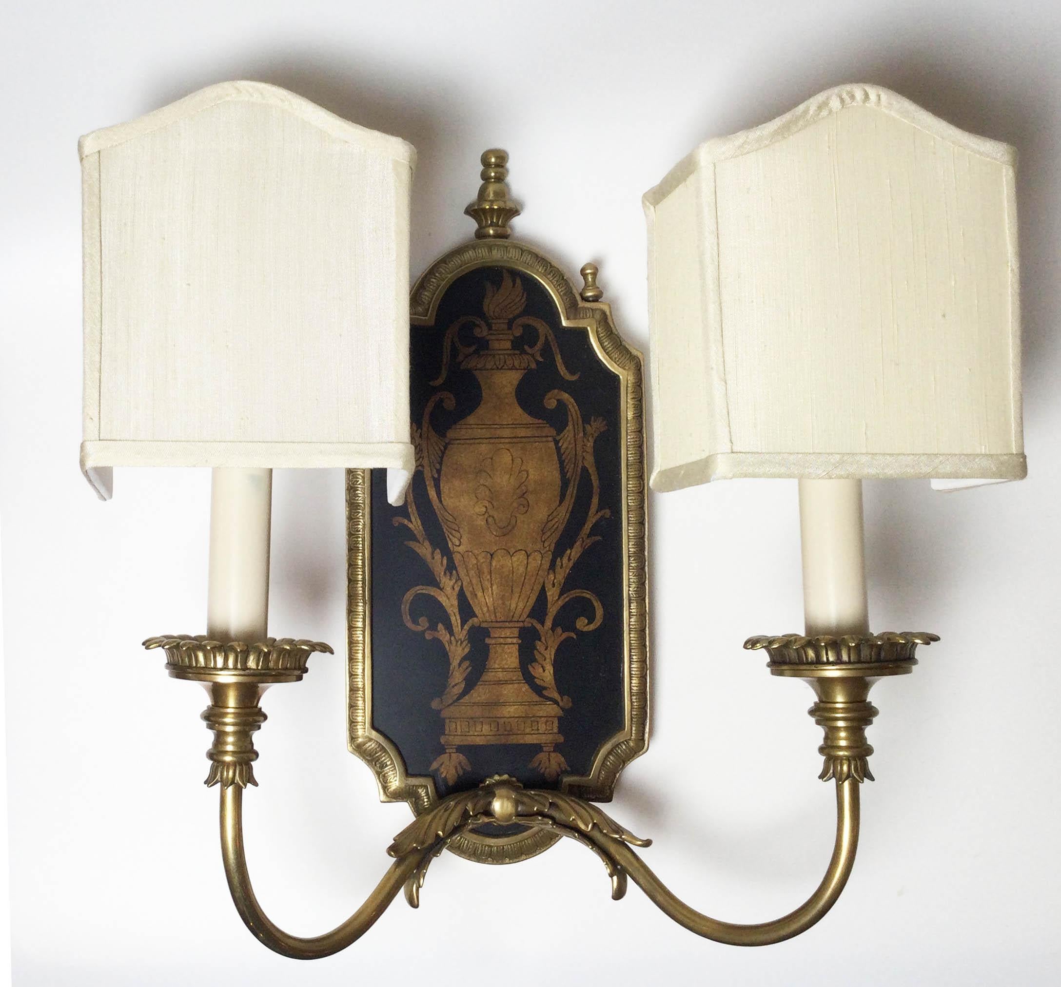 An elegant pair or antiqued brass two light sconces with wood panel back plate with urn design. Complete with four box shaped shantung silk shades . These are modern new wiring. measures 15.5 tall, 14.5 wide (with shades) 6.5 deep. 13 inches wide
