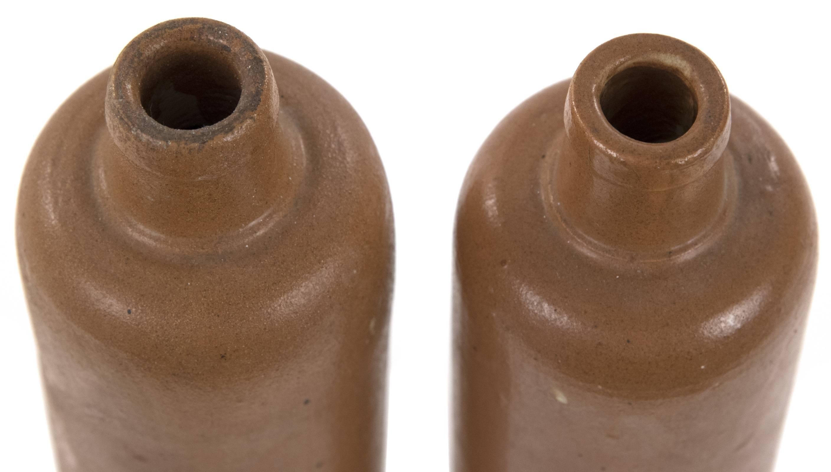 A pair of elongated brown glazed bottles with bottle necks, inscribed with the initials 