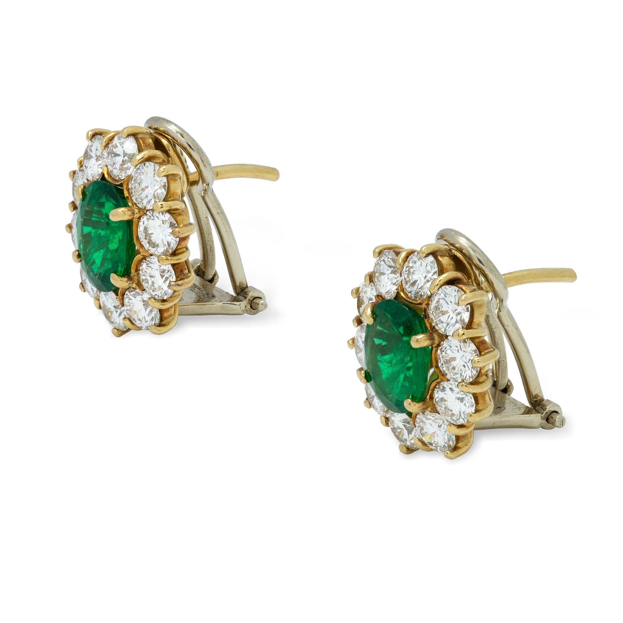 A pair of emerald and diamond cluster earrings, each earring centrally set with an oval faceted emerald, surrounded by ten round brilliant-cut diamonds, the emeralds estimated to weigh approximately a total of 1.85 carats and the diamonds