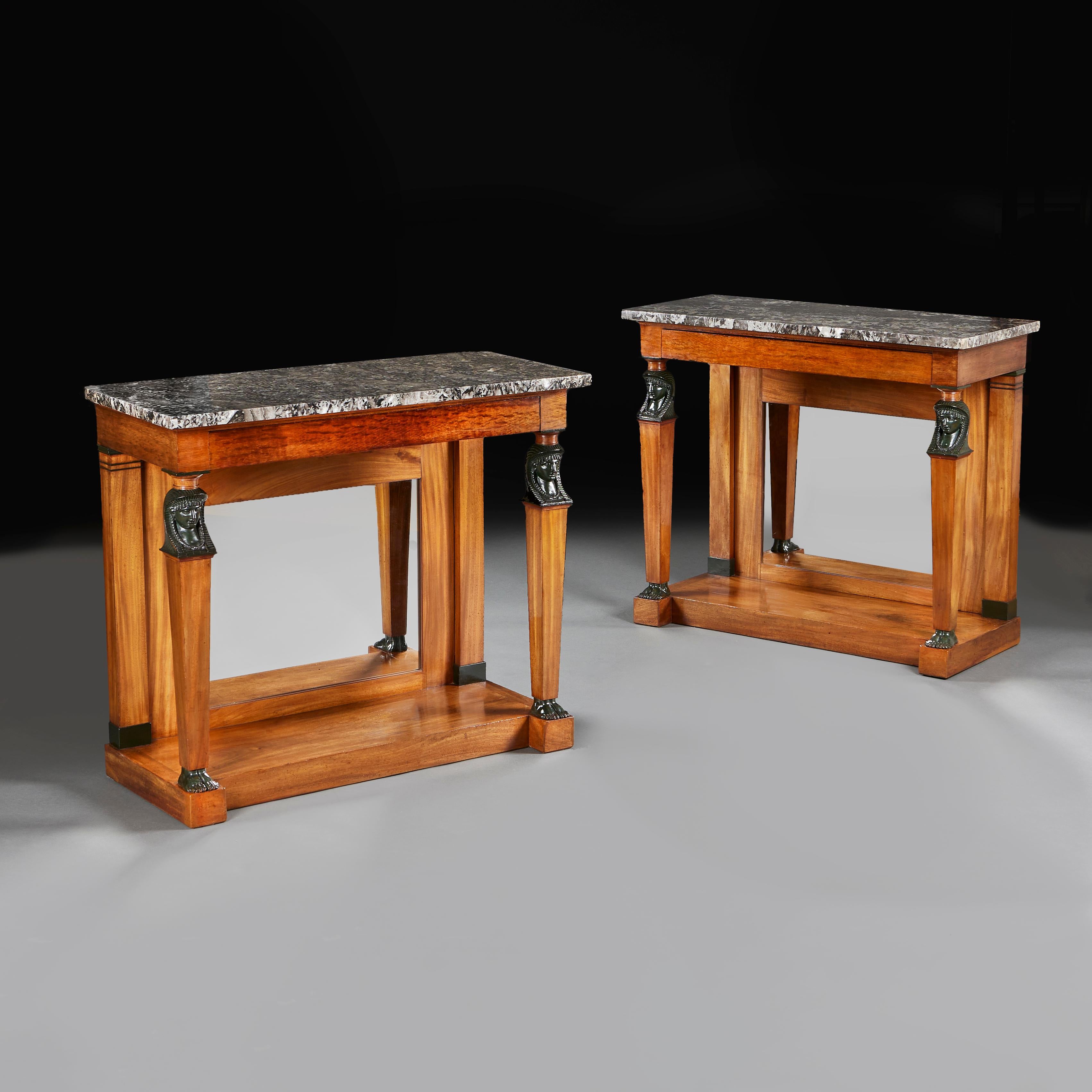 A fine pair of early nineteenth century Empire console tables of faded Honduran mahogany, retaining the original inset mirrored backs, the supporting legs with finely carved Egyptian caryatids to the top, tapering down to delicate feet at the base,