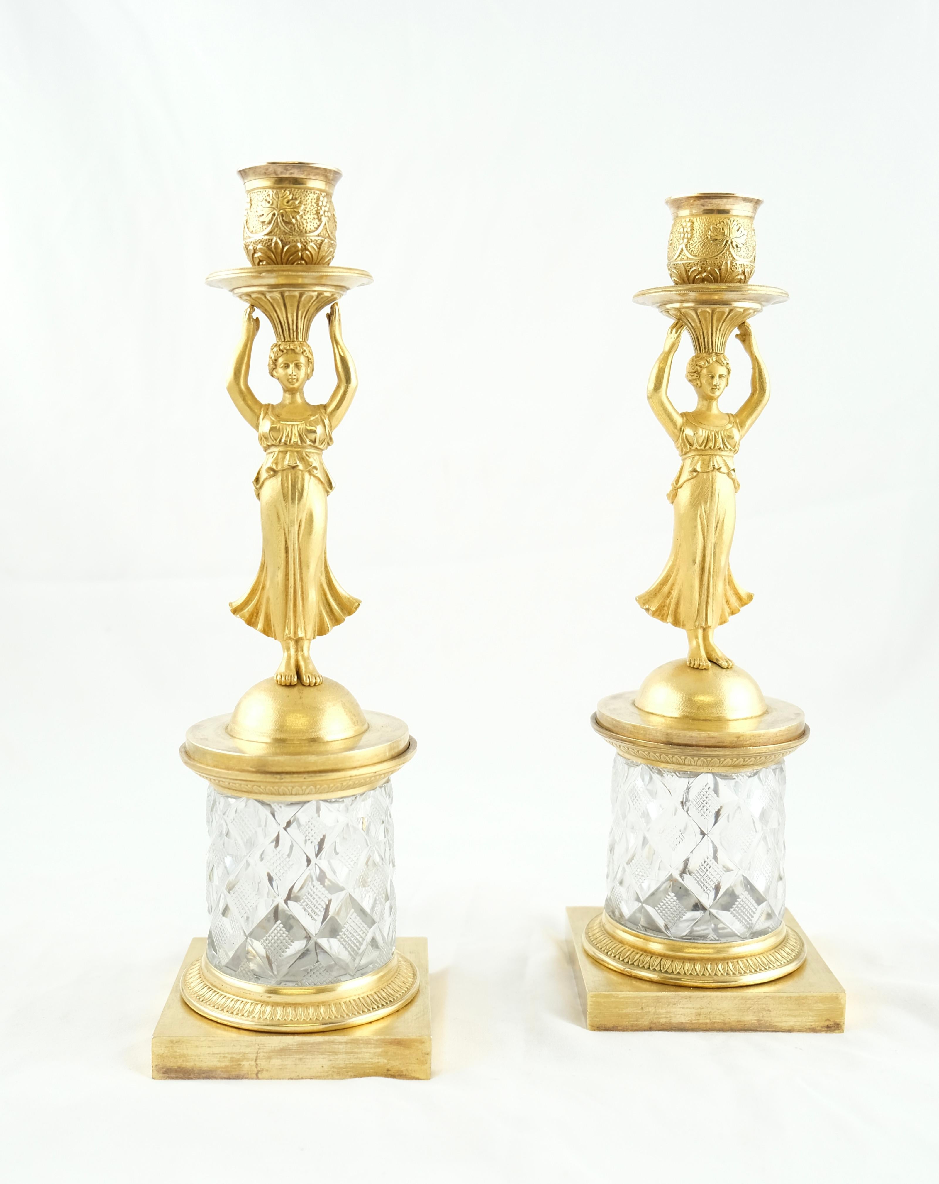 Une charmante paire de chandeliers. La plupart des chandeliers fabriqués durant cette période, Louis XV, Directoire et Empire, utilisent des bronzes qui sont soit dorés, soit patinés. Ces chandeliers ont des bases en cristal taillé, ce qui les rend