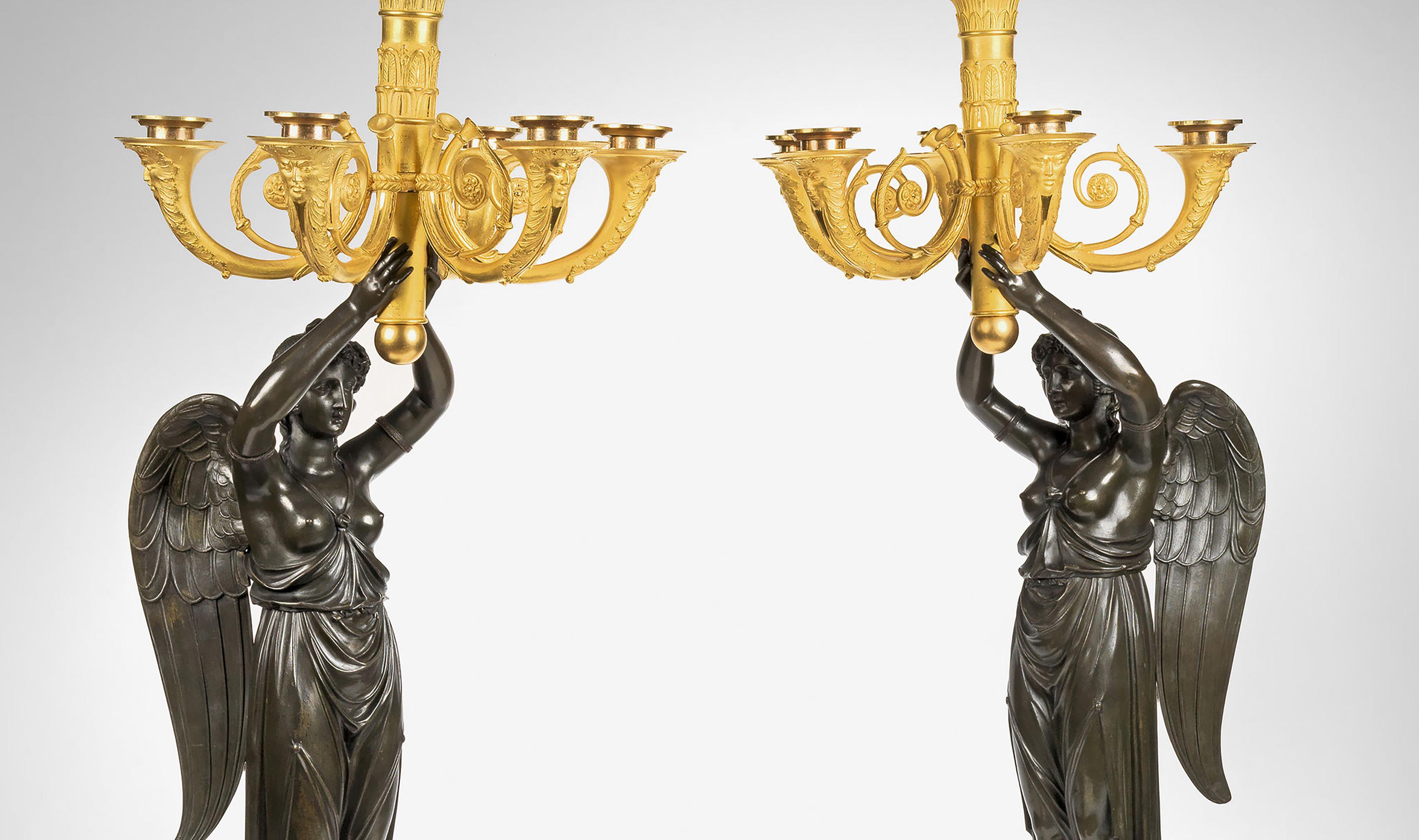 The five-light candelabra are each modelled as figures of winged victory holding a quiver of arrows issuing five musical Horn-shaped branches, on a square red marble base with circular ormolu wreaths with an ormolu ribbon and bow on all four