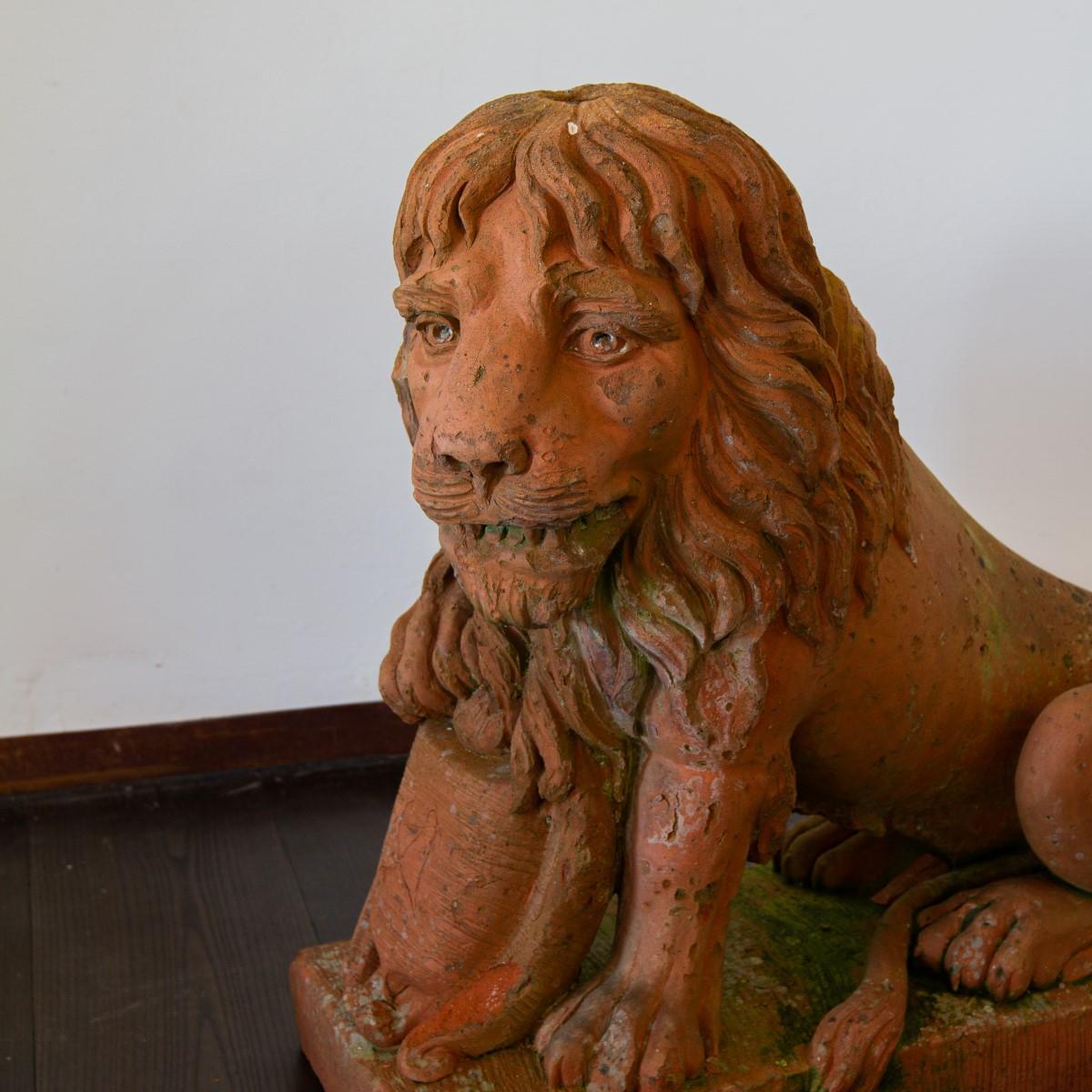 A pair of English 19th century beautifully weathered terracotta opposing seated lions with paws resting upon carved shields.