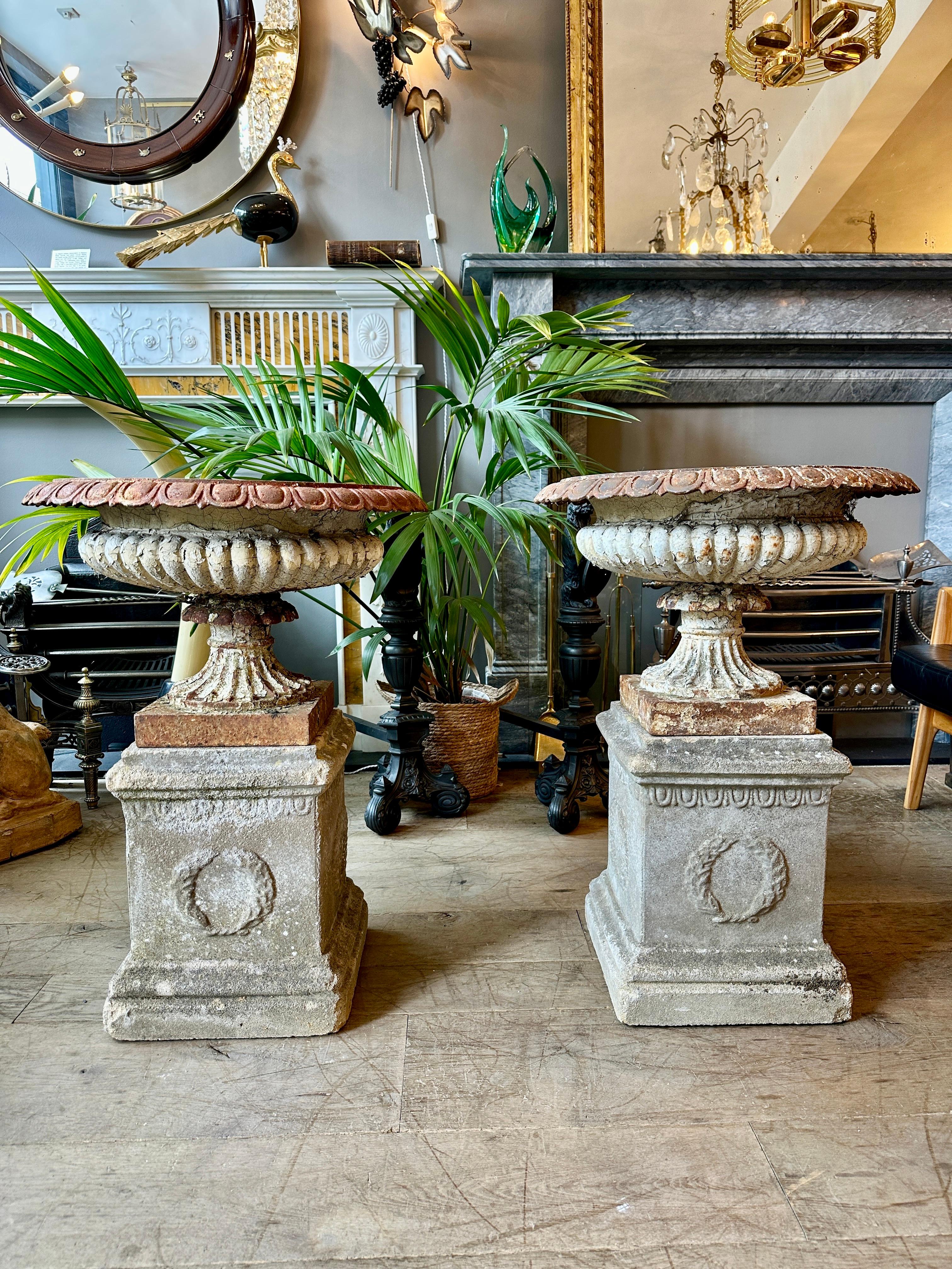 A wonderfully weathered pair of No.9 Tazza urns by renowned foundry Andrew Handyside. A wide and shallow saucer shaped bowl edged in egg and dart sits above the gadrooned body supported by a fluted spreading socle. Both urns supported by a stone