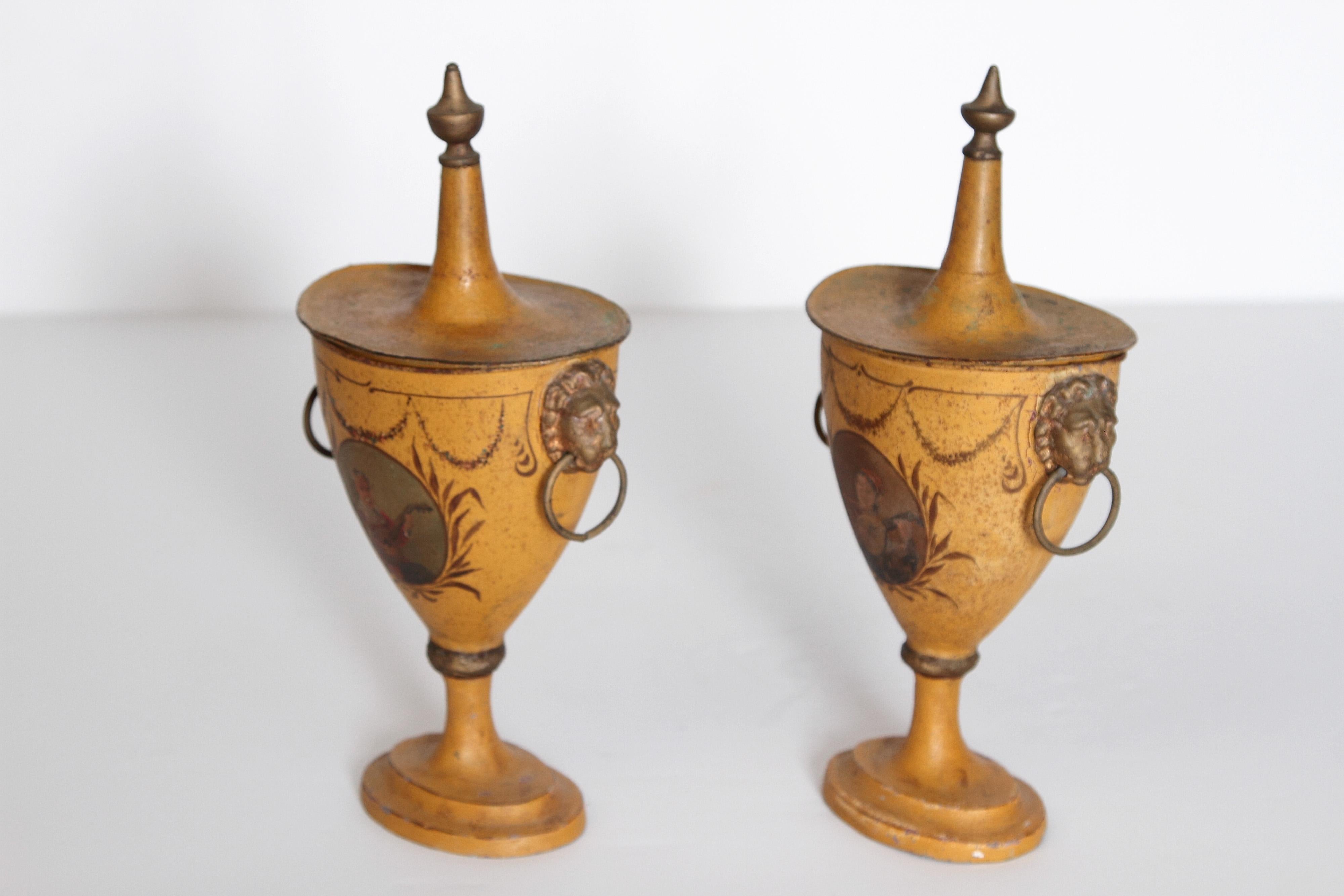 A pair of Regency tole painted chestnut urns with lids. Each tapering form is decorated with images of figures with instruments after the style of the Old Dutch Masters. Reserved on a mustard yellow ground with floral swags. On the sides are lion