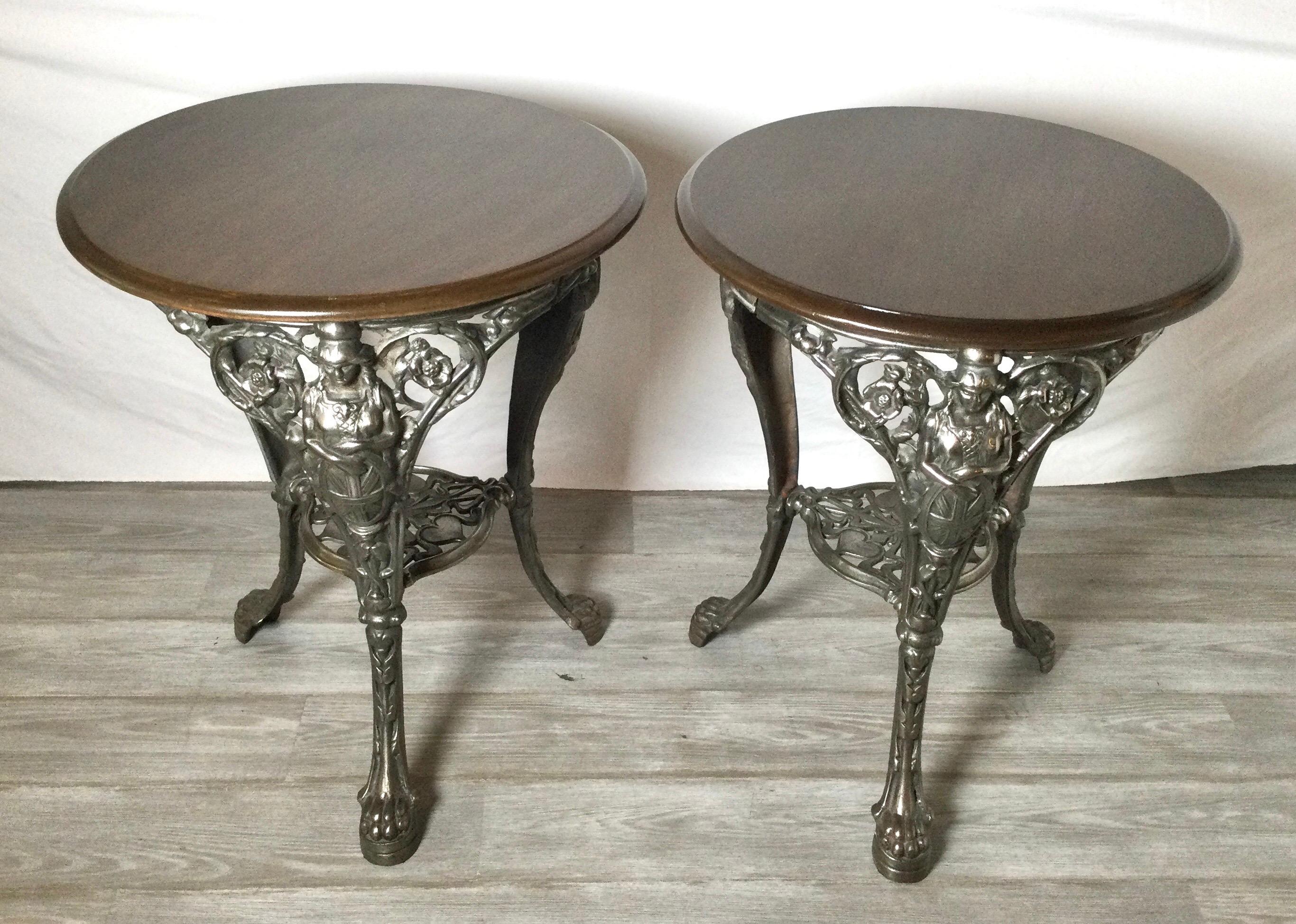 A pair of cast iron round pub tables with newer hardwood tops. The tables from 1875 with the old painted surface polished to the original iron finish. These table with figurative legs and thee paw feet.
