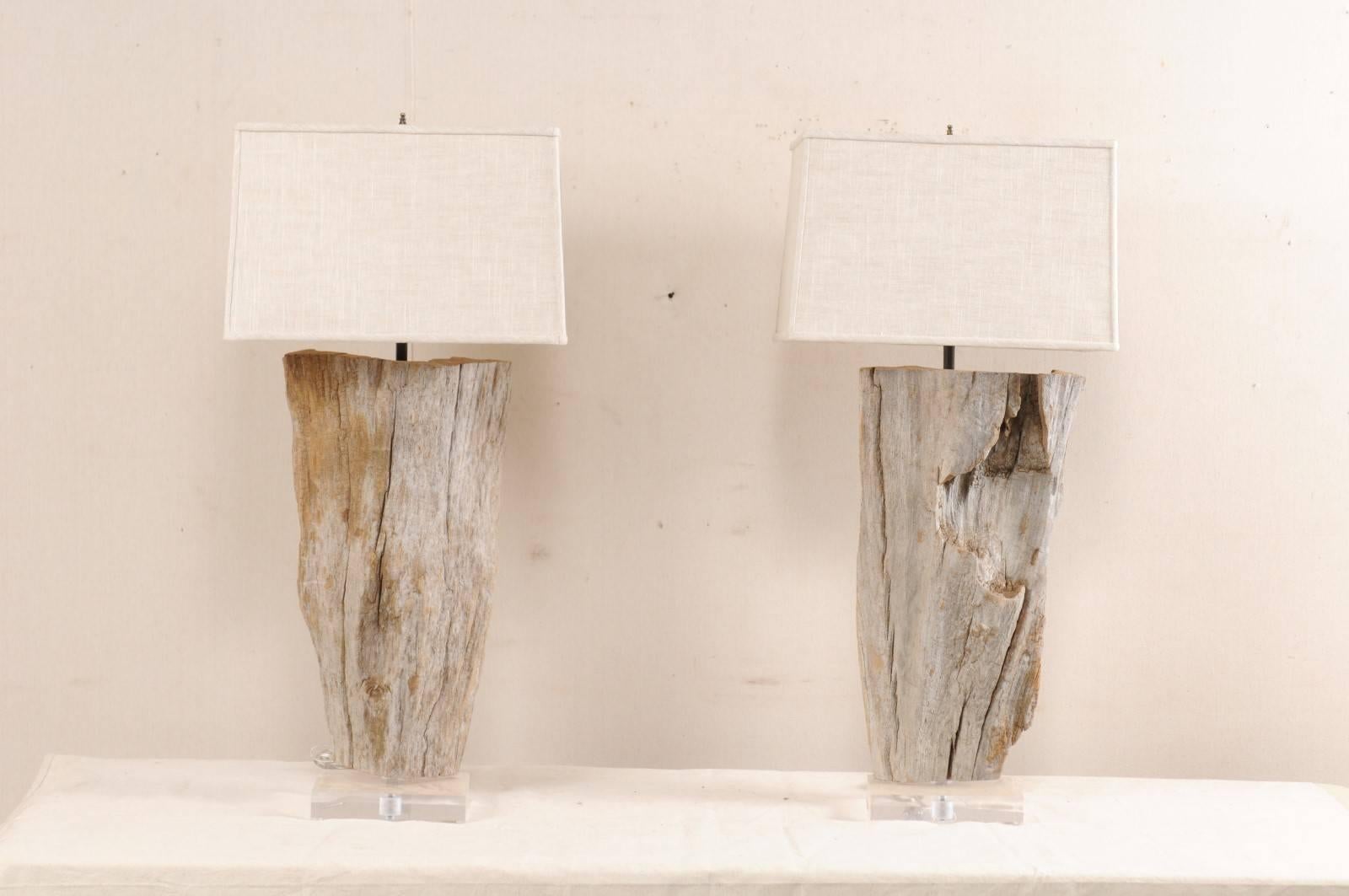 A pair of custom European natural wood and Lucite table lamps. This pair of European lamps each feature a natural piece of wood, with a beautiful driftwood finish, which has been mounted and raised on custom Lucite bases. The lamps come with