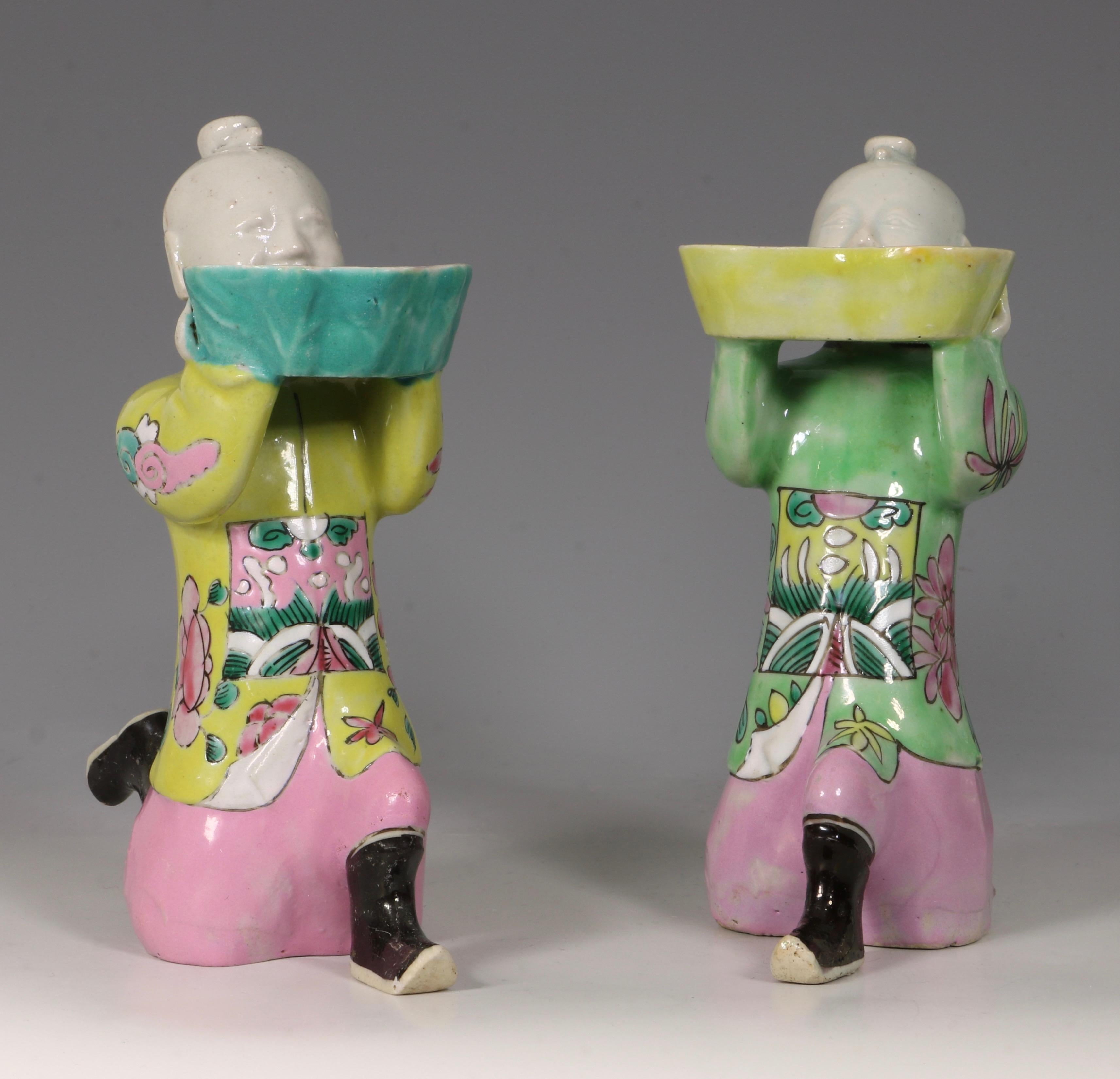 A pair of Famille Rose figures of kneeling boys as water droppers 18th-19th century.
One with a yellow and the other with a green robe, both with pink trousers.
Each with a hole at the back of the head and supporting a shaped bowl containing an
