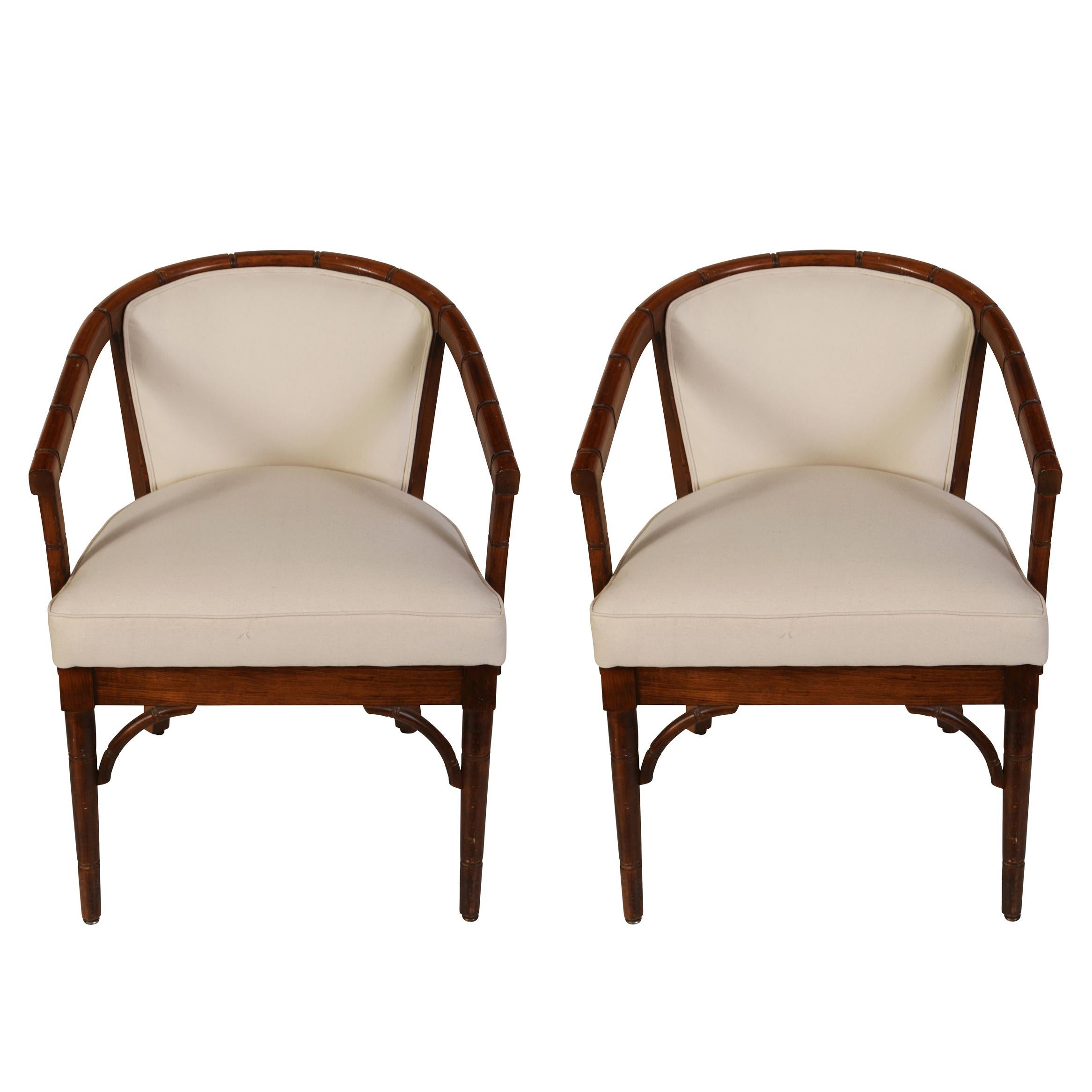 Ein stilvolles Paar Armlehnstühle aus Bambusimitat mit einer geschwungenen, festen Rückenlehne, einem festen Sitz und einem schönen Detail an der Schürze und an der Basis des Sitzes.  In schlichtem weißen Musselin gehüllt, ist dieses Duo bereit für