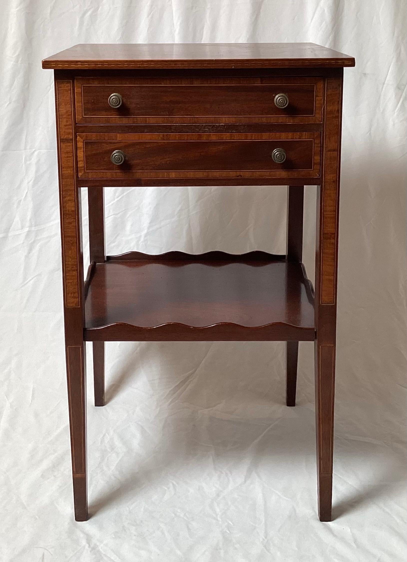 A pair of Federal style Mahogany side tables with cross banding trim.  The top with two slender drawers with antiques brass pulls on tapering legs with a lower shelf with scalloped gallery edge.  A nice diminutive size, 29 inches tall, 17.5 inches