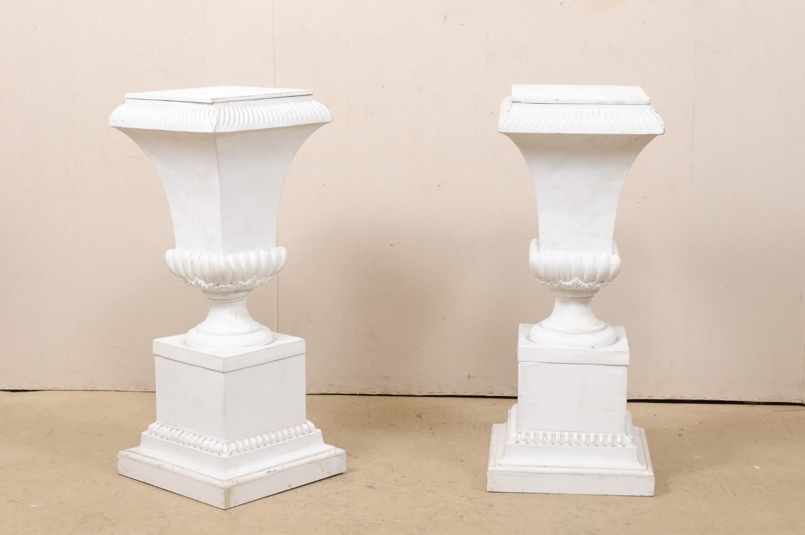 A pair of vintage American fiberglass pedestals. This pair of pedestals each stand approximately 3.75 feet in height, feature urn-shaped bodies with egg-and-dart and foliage adornment, and raised upon stacked square shaped bases. The urns are