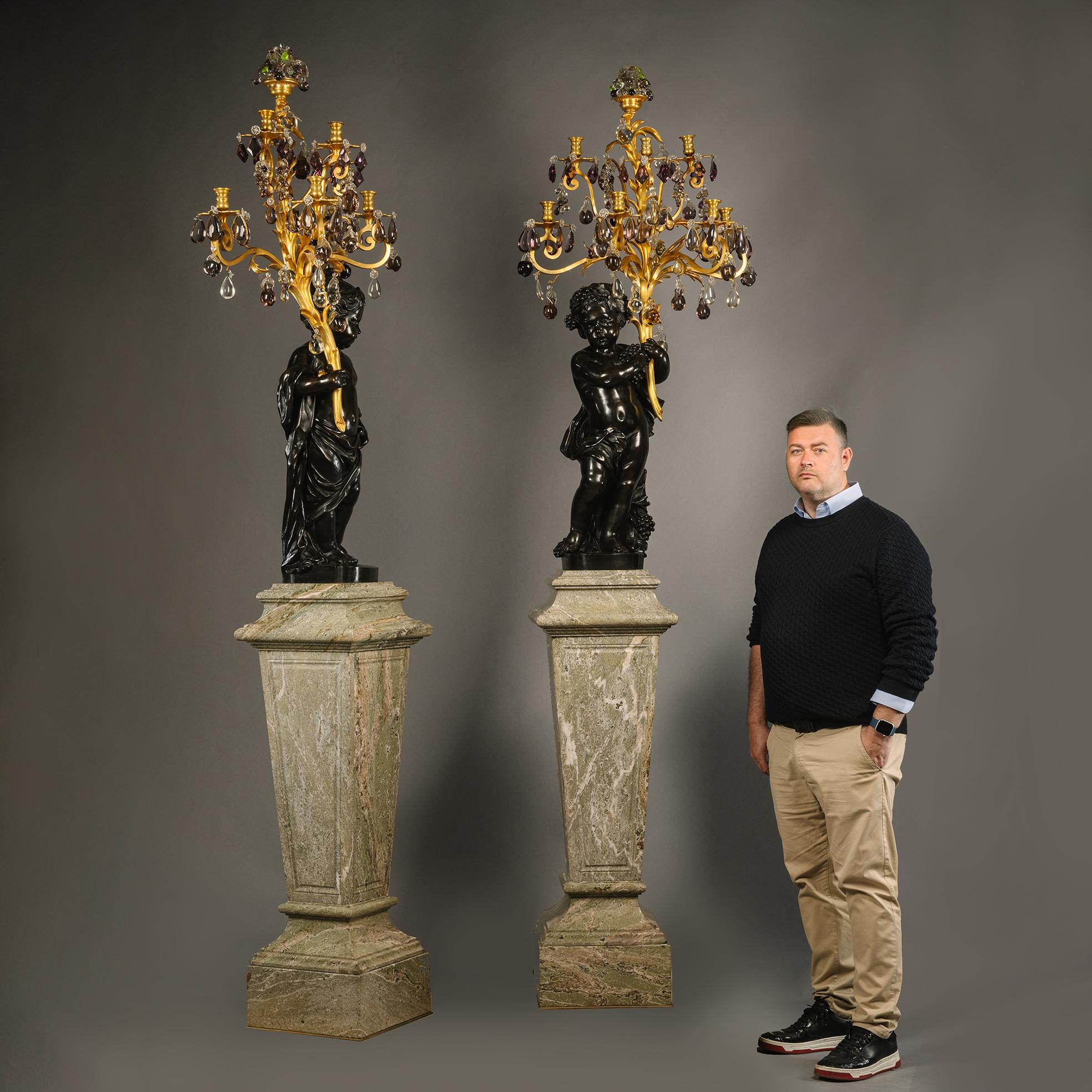 A Pair of Magnificent and Palatial Patinated Bronze Figural Putto Seven-Light Gilt-Bronze, Rock-Crystal and Amethyst Glass Candelabra, On Green Marble Pedestals. 

By Raingo Frères, Paris. 

Incised 'RF' marks for Raingo Frères. 

These magnificent