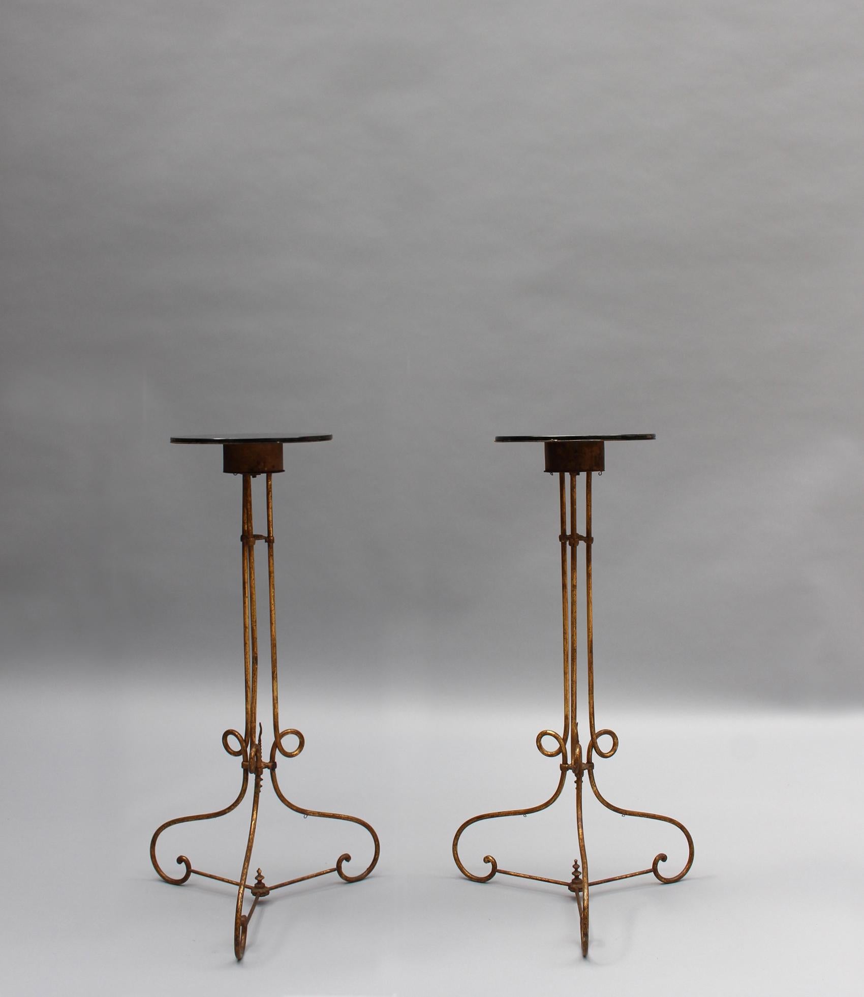 A pair of fine and elegant French Art Deco pedestal stands with a gilded wrought iron base that supports a black opaline glass top (which diameter is 10 1/4
