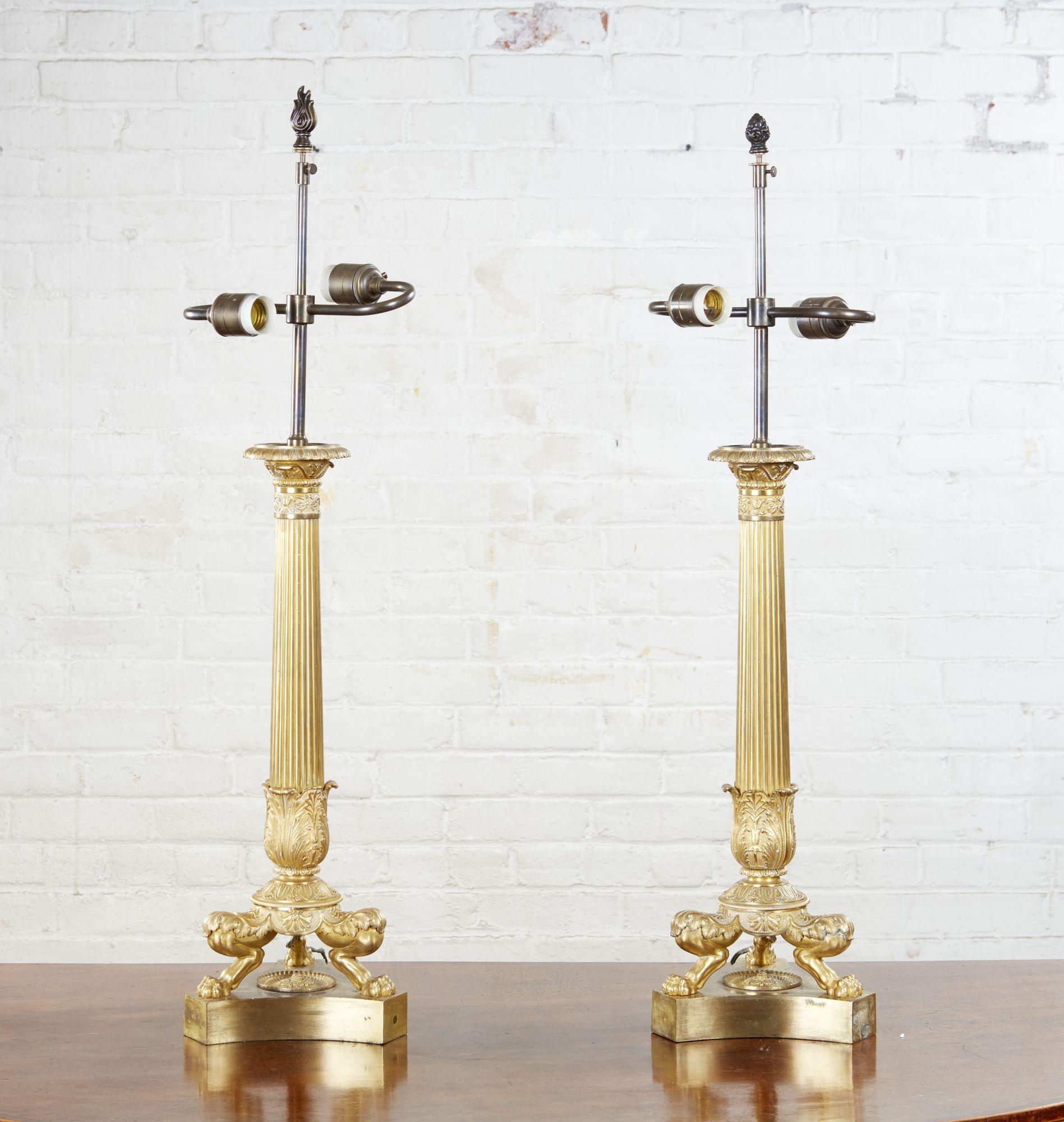 A pair of early 19th century bronze and firegilt candelabrum, now fitted and wired as lamps, with finely chased detail, featuring tapered fluted columns surmounted by an egg and dart decorated capital and with a tulip shaped column mount, over three