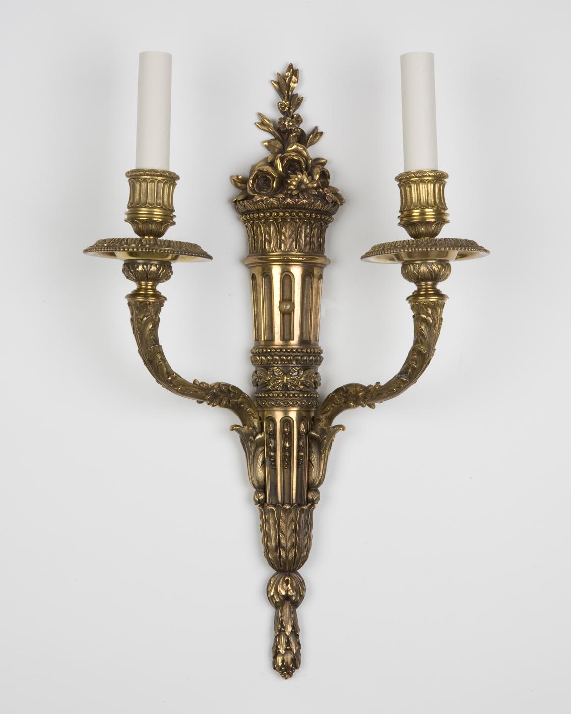 AIS2576
A pair of two arm sconces with very finely chased foliate details. Having slender backplates topped with a bouquet of flowers. In their original age-darkened brass finish by the New York maker E. F. Caldwell Co. Circa