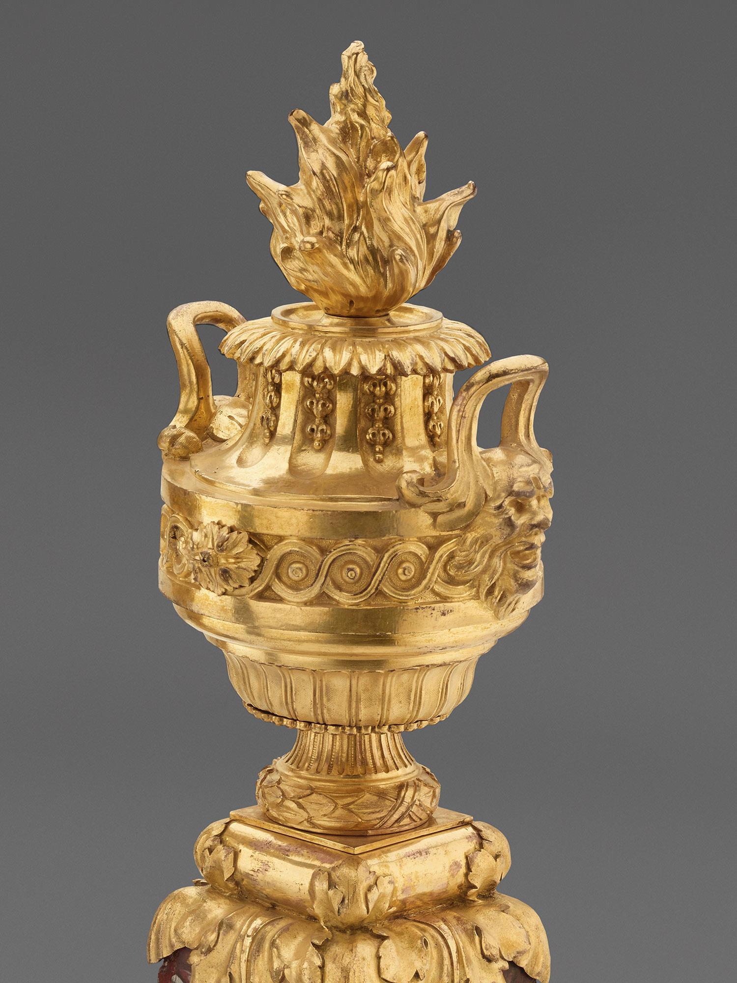 Paris, c. 1760
Attributed to the workshop of Pierre Gouthière (1732-1813, master 1758). The bronze flaming urns with original fire gilding stand on stepped, dark red marble pedestals with pearl rod appliqué and overhanging acanthus foliage. The