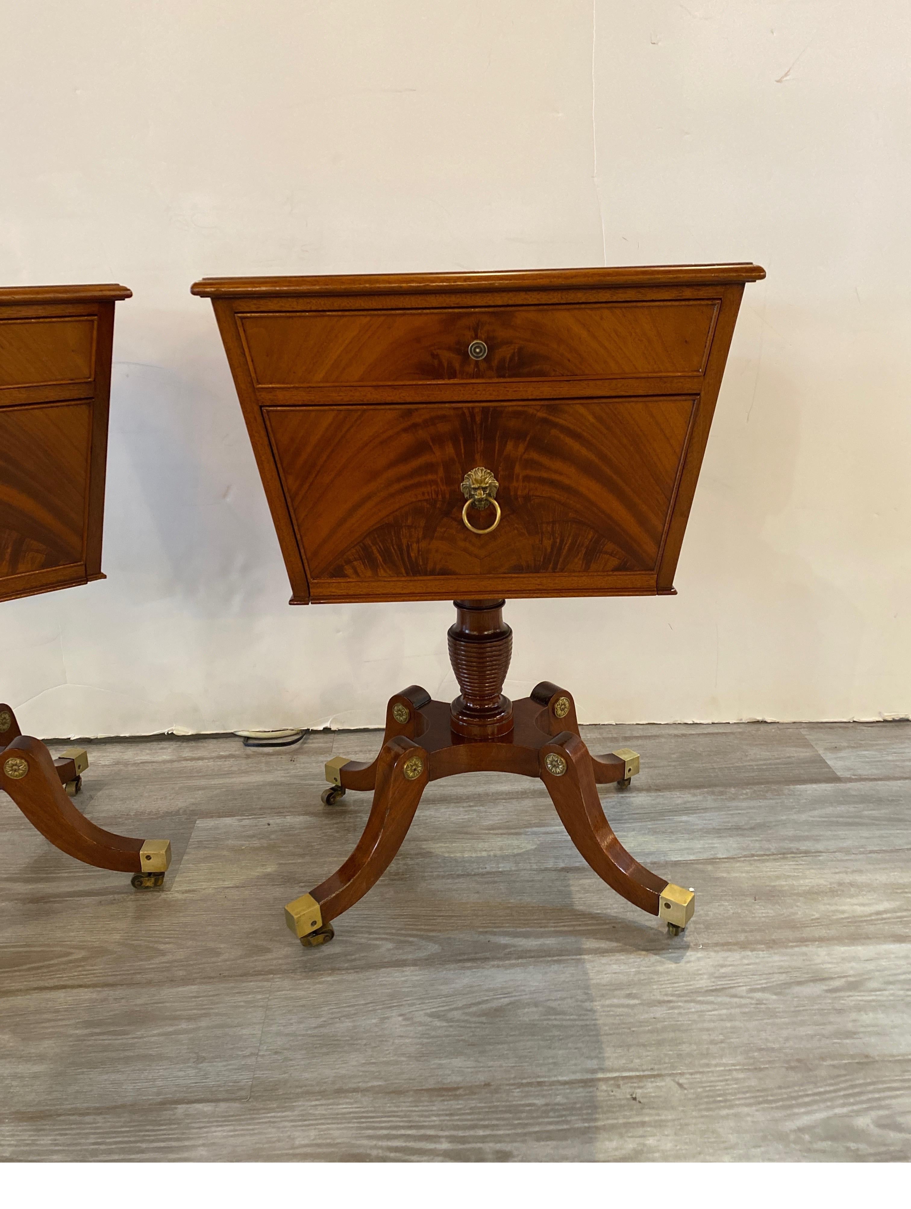 An elegant pair of Regency style flame mahogany pedestal cabinets. The warm mahogany with cast brass lion head accents on the sides and front with a pull down door for storage and top drawer. The cabinets on a center column with four brass capped