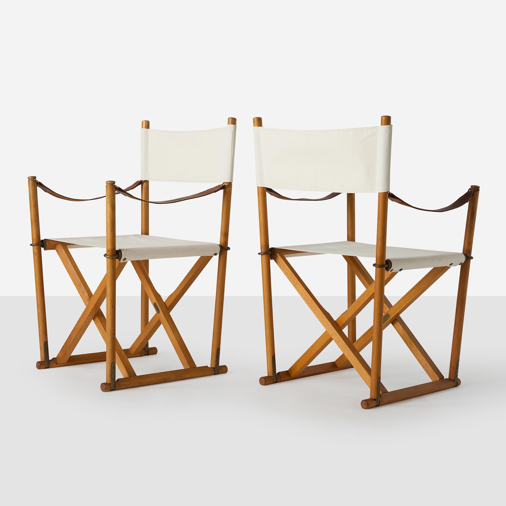 A pair of folding director's-style chairs of beech, brass, and canvas, with low-slung leather arms. Professionally restored with new canvas seats and backs.