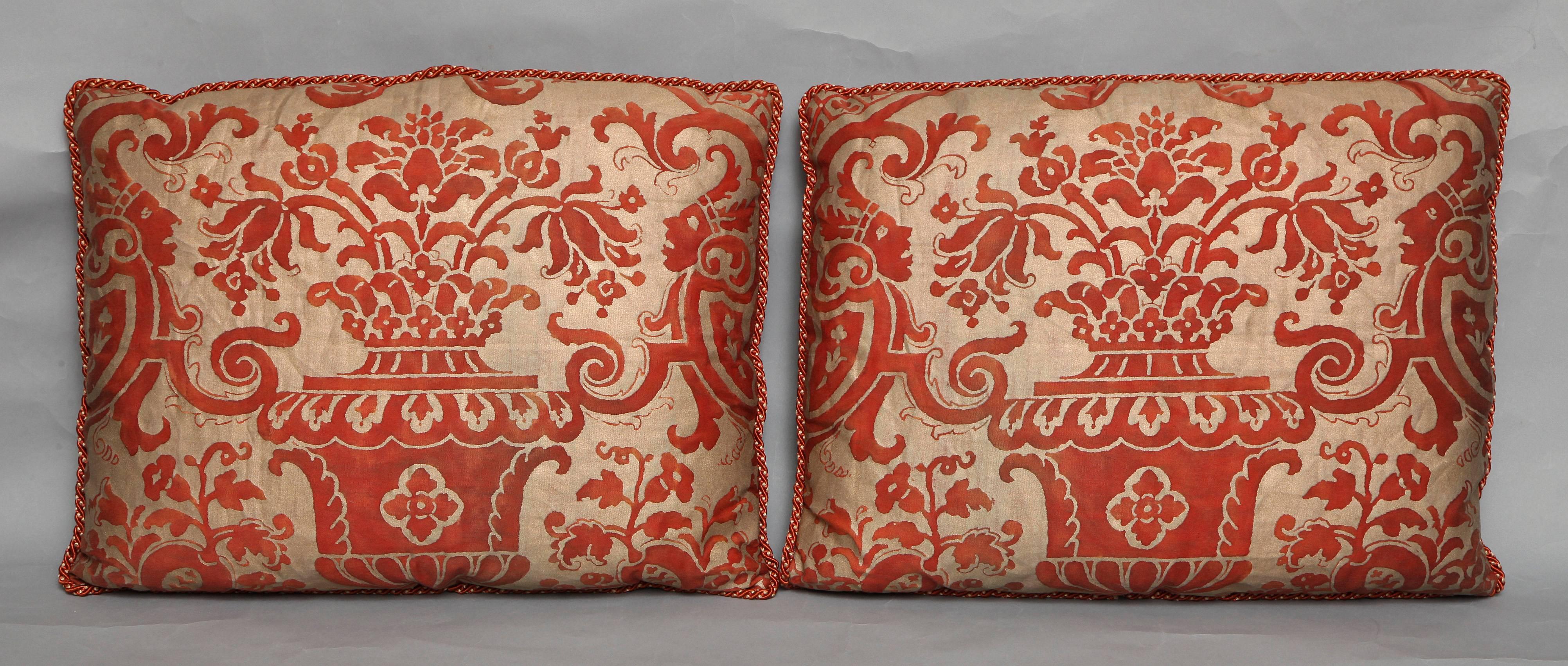 A pair of Fortuny fabric cushions in the Carnavalet pattern, rectangular shade in a silvery gold ground and red damask with linen backs and braided edging, the pattern, a 17th century French design named for the Carnavalet museum in Paris where