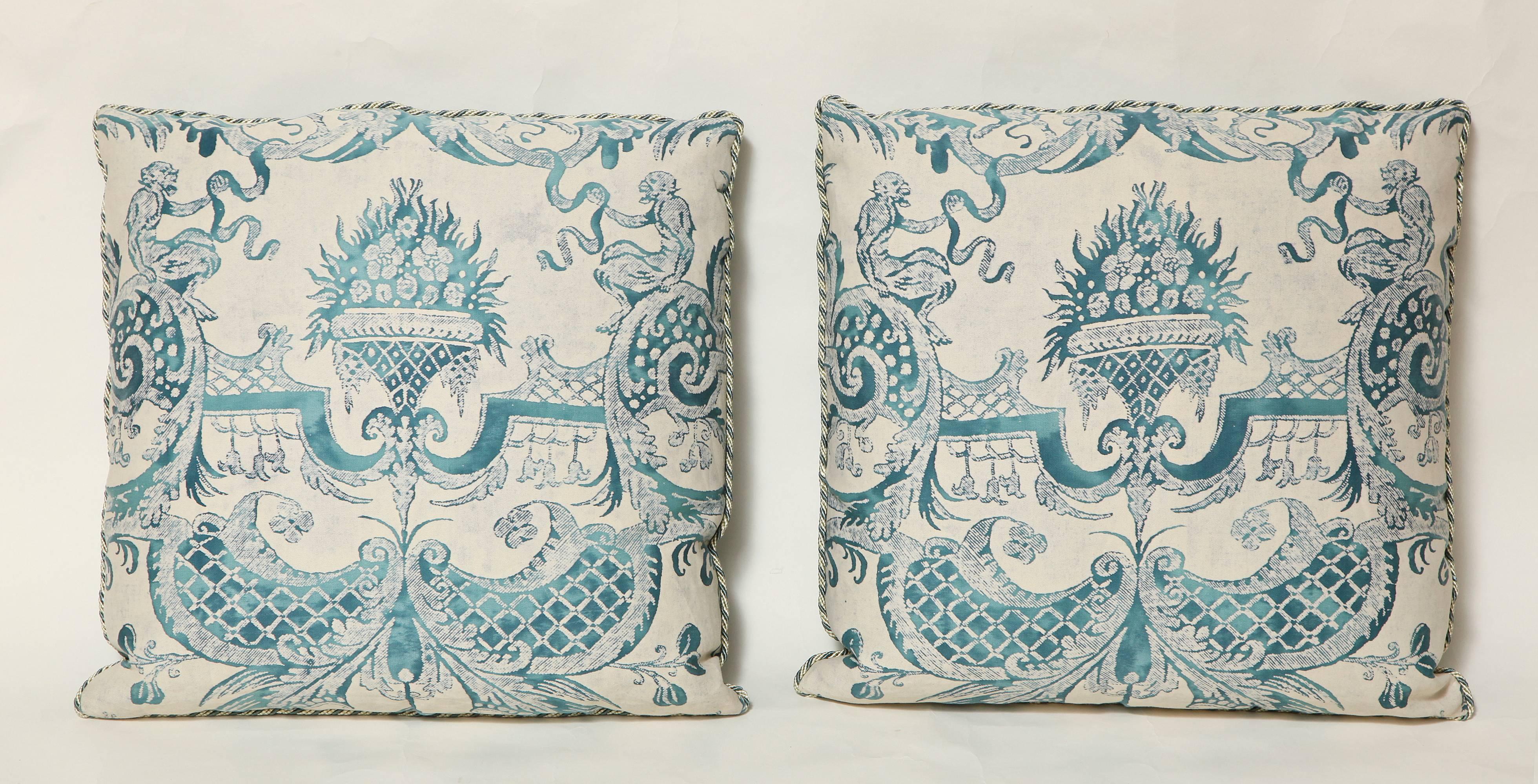 A pair of Fortuny fabric peacock blue and ivory Mazzarino pattern cushions with white and blue braided edging and grey/silver silk taffeta backs.