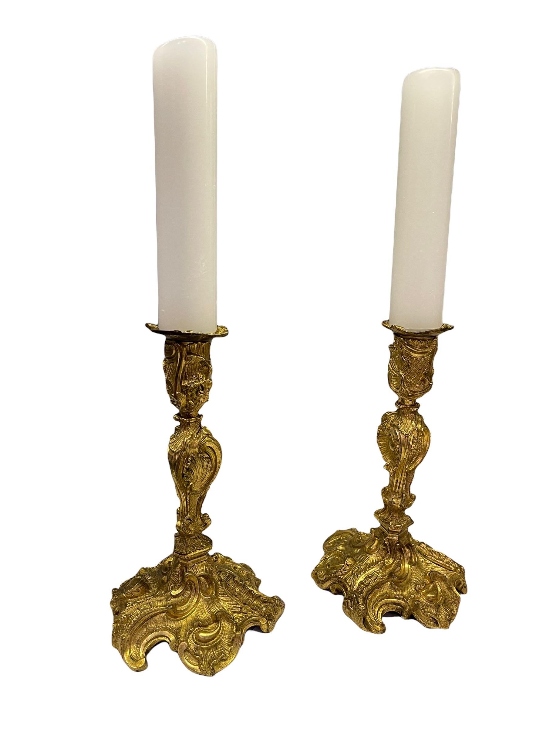 A pair French 18th Century bronze gold gilt candlesticks with the original drip catchers. The candle holders are decorated with sweeping scrolls in an organic composition A round base with stylized vines and scallops motifs. The seamed hollow stems