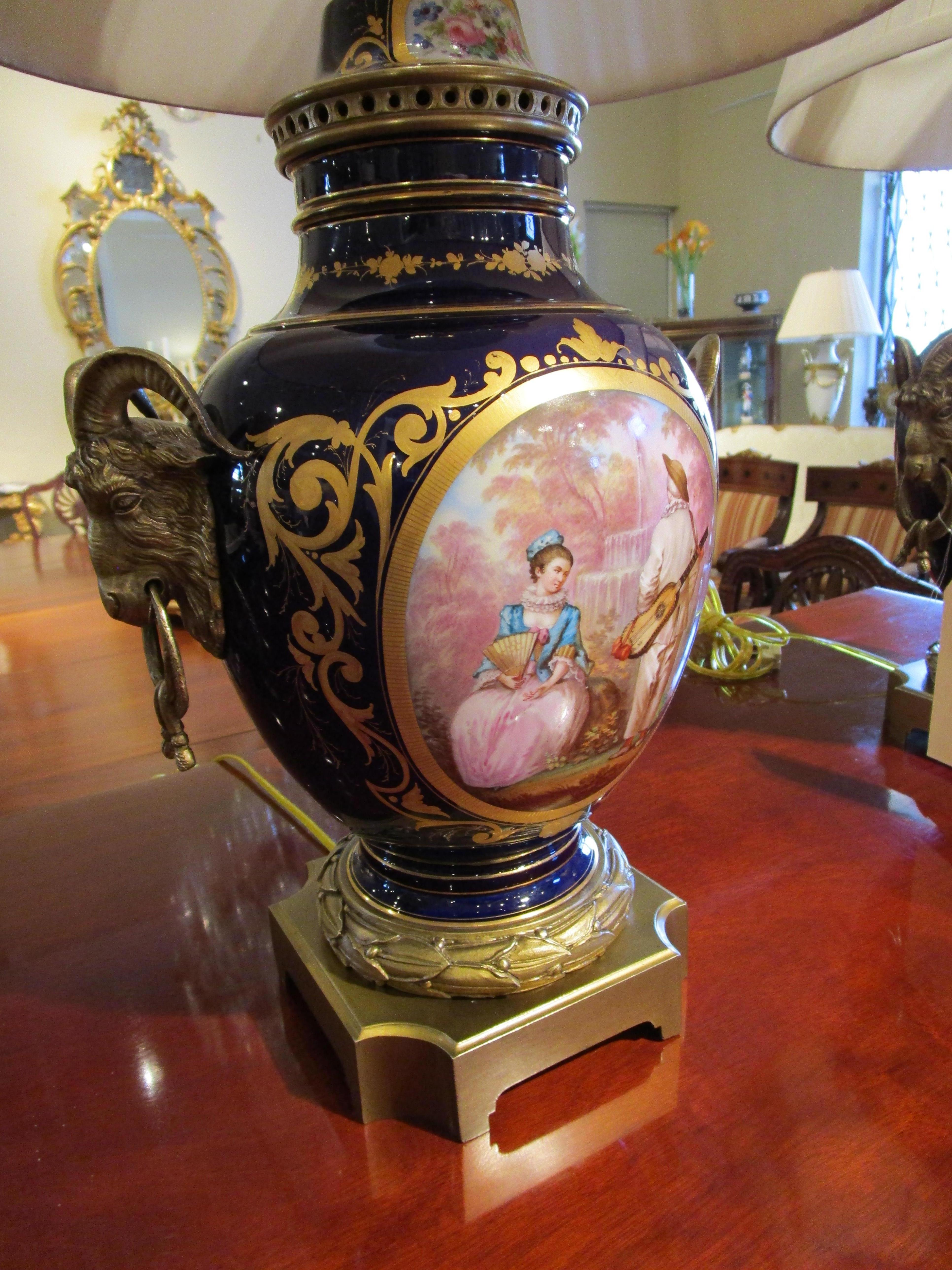 A fine pair of late 19th century French Louis XVI Sevre's style gilt bronze and cobalt porcelain hand painted and signed urns with gilt bronze ram's heads mounts. Custom wired and shaded.