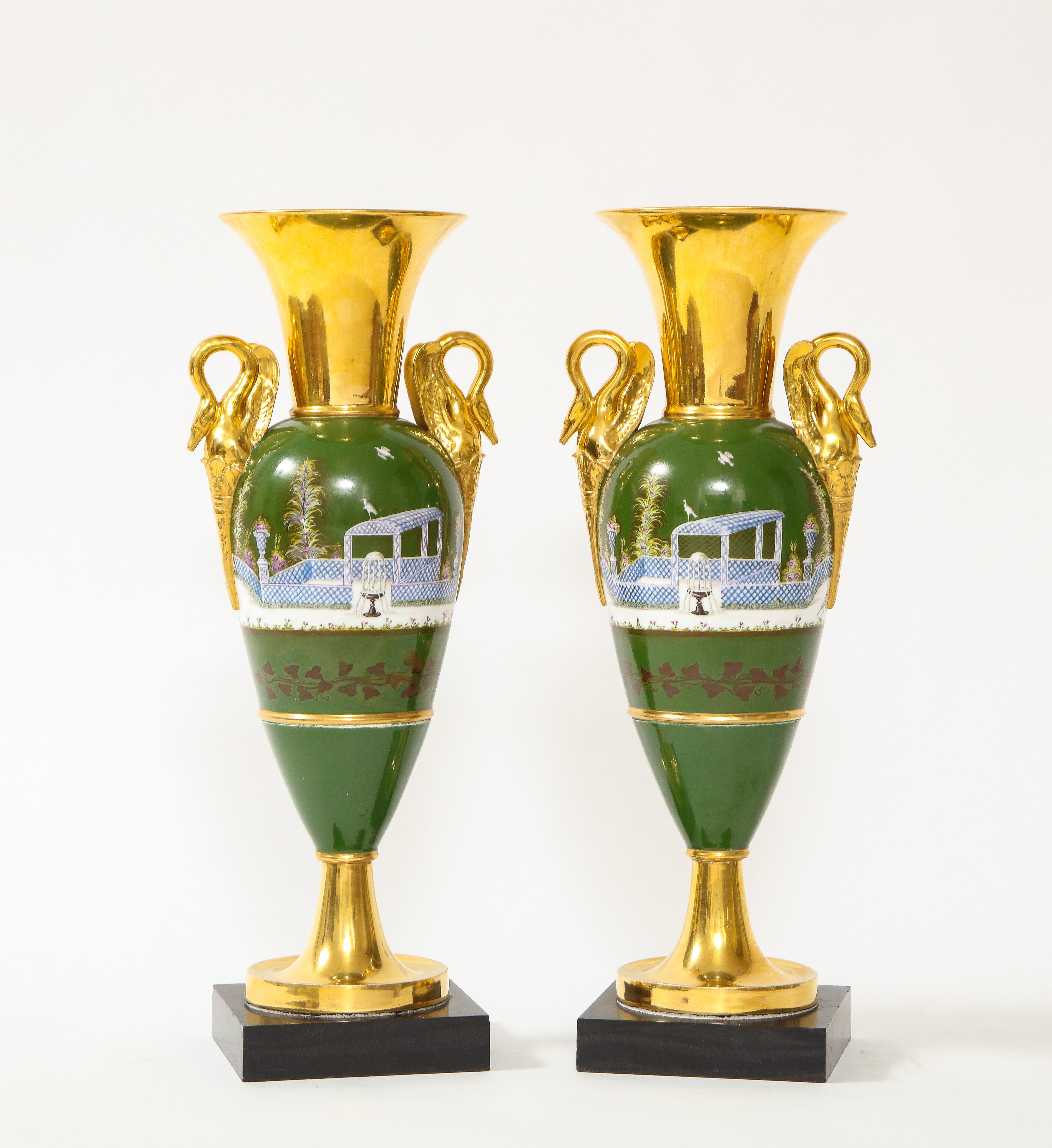 A fine pair of French 19th century Empire Period Old Paris porcelain swan handle vases. Each is beautifully hand-painted with a green colored ground and further adorned with 24K gold-painted accents around the neck, handles, and bases. The vases are