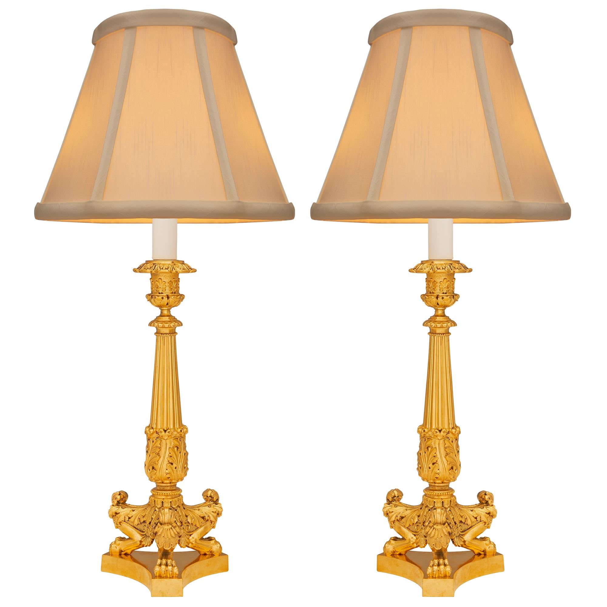 A striking pair of French 19th century Charles X st. ormolu candlestick lamps. Each lamp is raised by an elegant triangular base with concave sides below an impressive scrolled foliate support with finely detailed acanthus leaves, palmettes, and