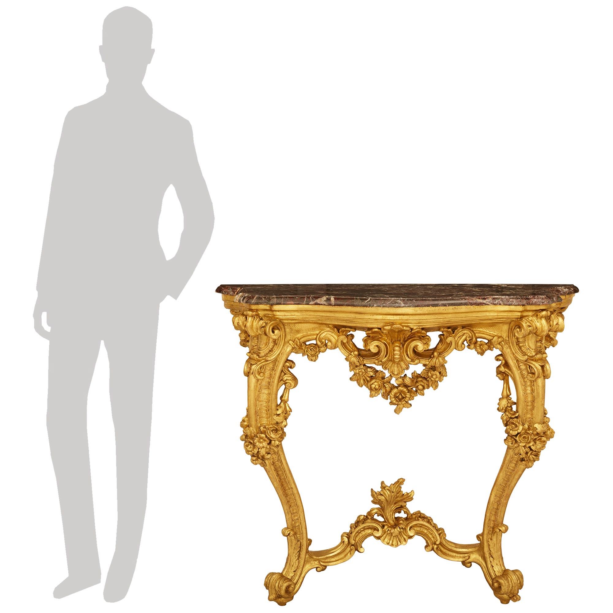 Pareja elegante y de gran calidad de consolas francesas del siglo XIX de estilo Luis XV ricamente talladas en madera dorada y mármol Rosso Levanto. Cada una de las impresionantes consolas se eleva sobre un par de patas de acanto con roleos que