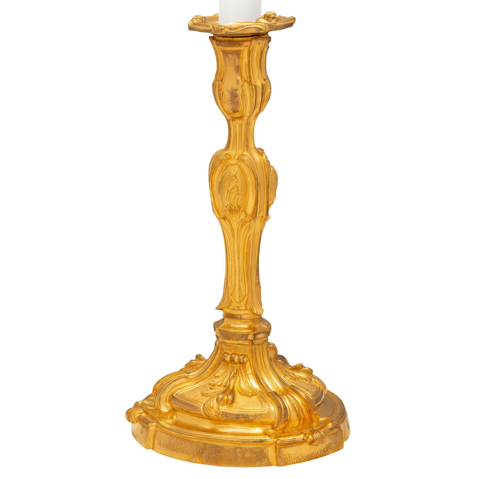 Un'elegante coppia di candelabri francesi del XIX secolo in stile Luigi XV montati in lampade. Ogni lampada è sollevata da una base circolare con tre sottili elementi sporgenti al di sotto di graziosi disegni fogliacei a volute in una ricca finitura