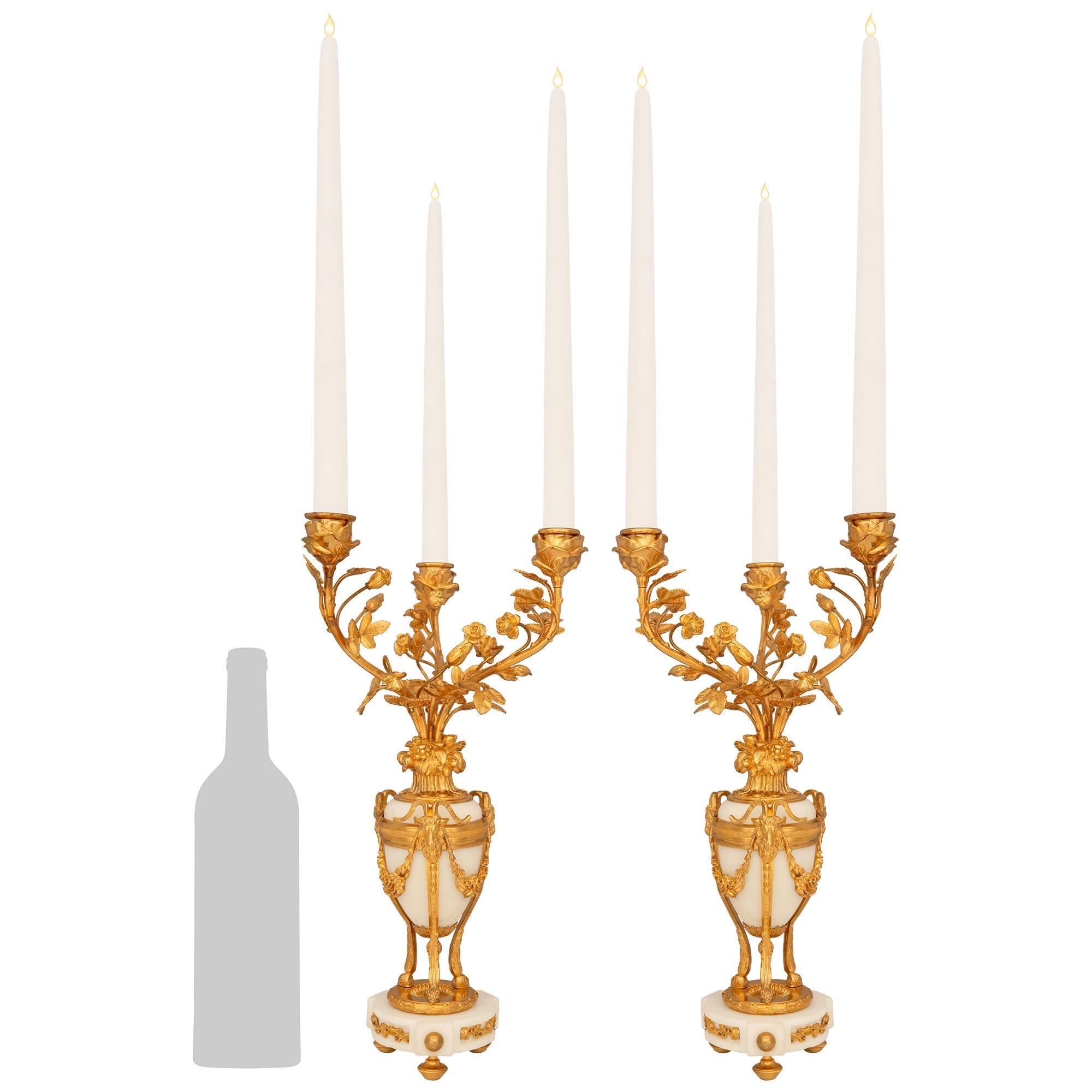 Una splendida ed elegante coppia di candelabri francesi del XIX secolo in stile Luigi XVI in ormolu e marmo bianco di Carrara. Ogni bellissimo candelabro a tre bracci è montato su una base circolare in marmo che presenta tre pannelli rientranti con