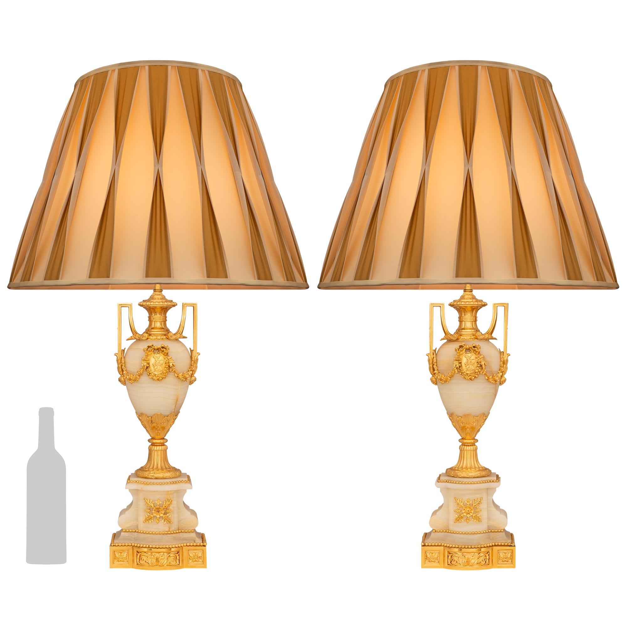 Un'attraente ed elegante coppia di lampade francesi del XIX secolo in onice e ormolu di stile Luigi XVI. Ogni lampada, davvero straordinaria, è sollevata da una base in onice screziata e a gradini con una riserva frontale floreale a bacche traforate