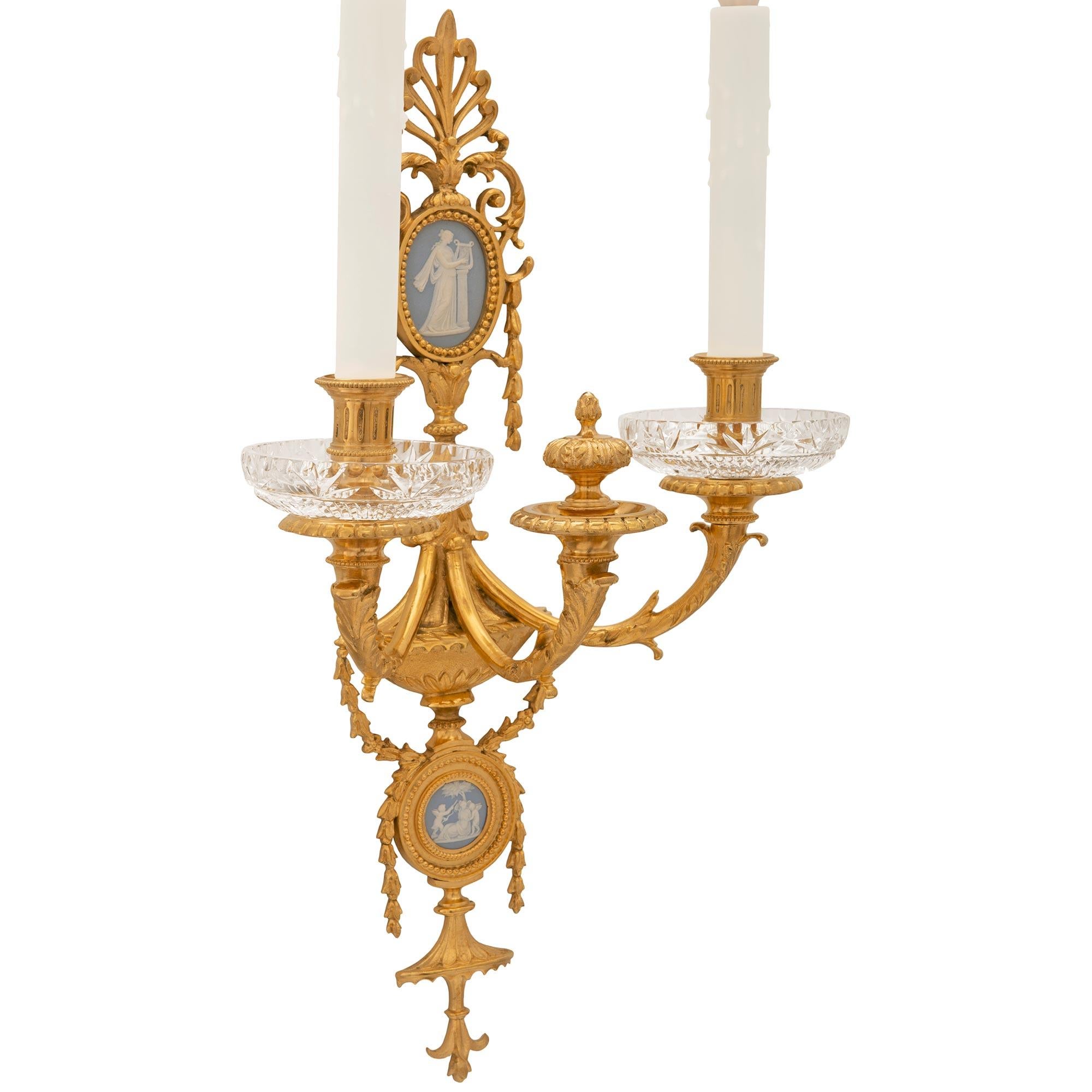 An elegant pair of French 19th century Neo-Classical st. Ormolu, Wedgwood porcelain and crystal sconces. Each three arm sconce displays a bottom reserve with draped foliate garlands centered by a Wedgwood porcelain medallion. One sconce depicts a