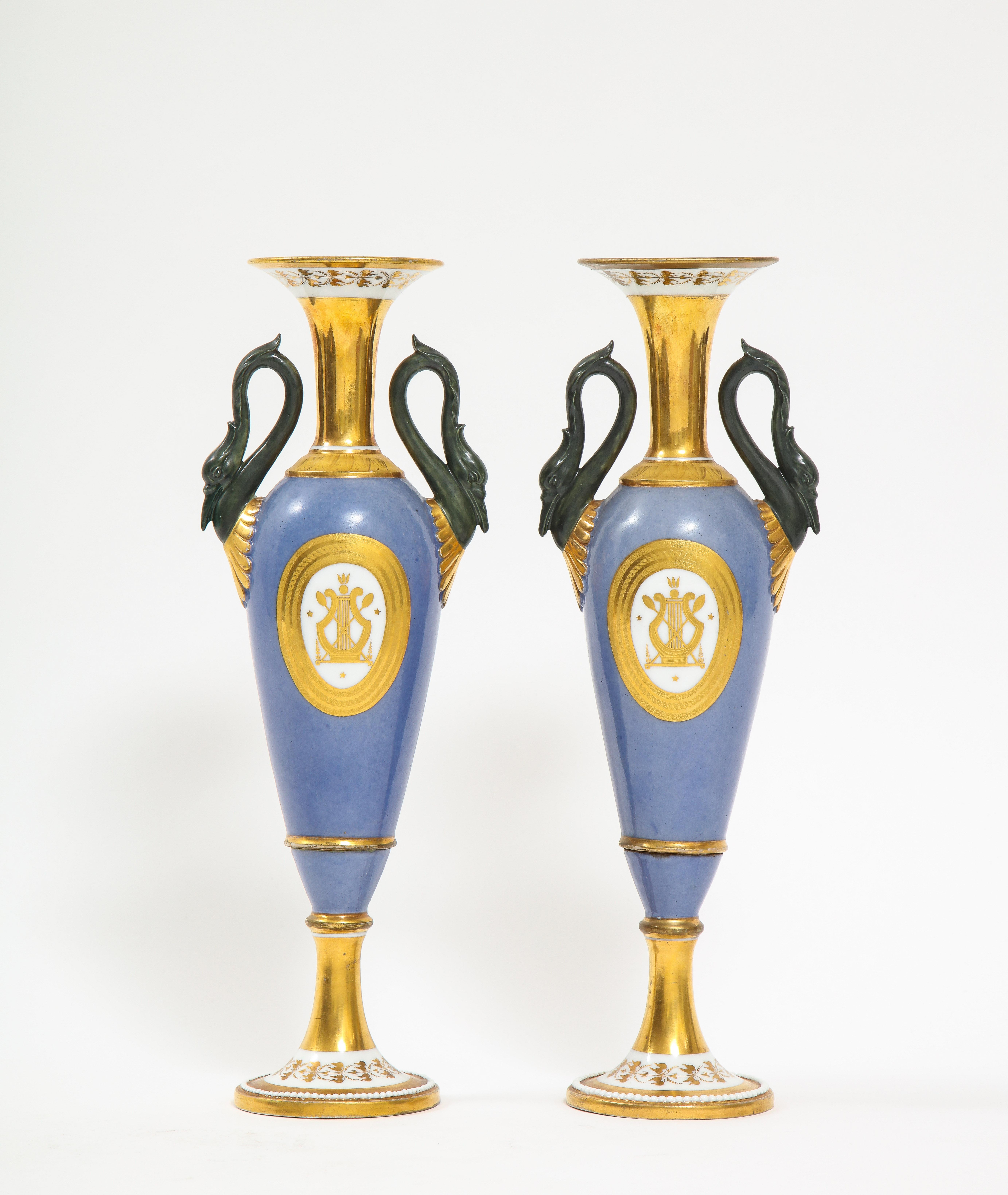 Ein feines Paar französischer Vasen mit Schwanenhenkel aus dem Empire des 19. Jahrhunderts aus altem Pariser Porzellan. Jede ist wunderschön handbemalt mit einem hellblauen Grund und zusätzlich mit 24-karätigen Goldakzenten um den Hals, die Griffe,